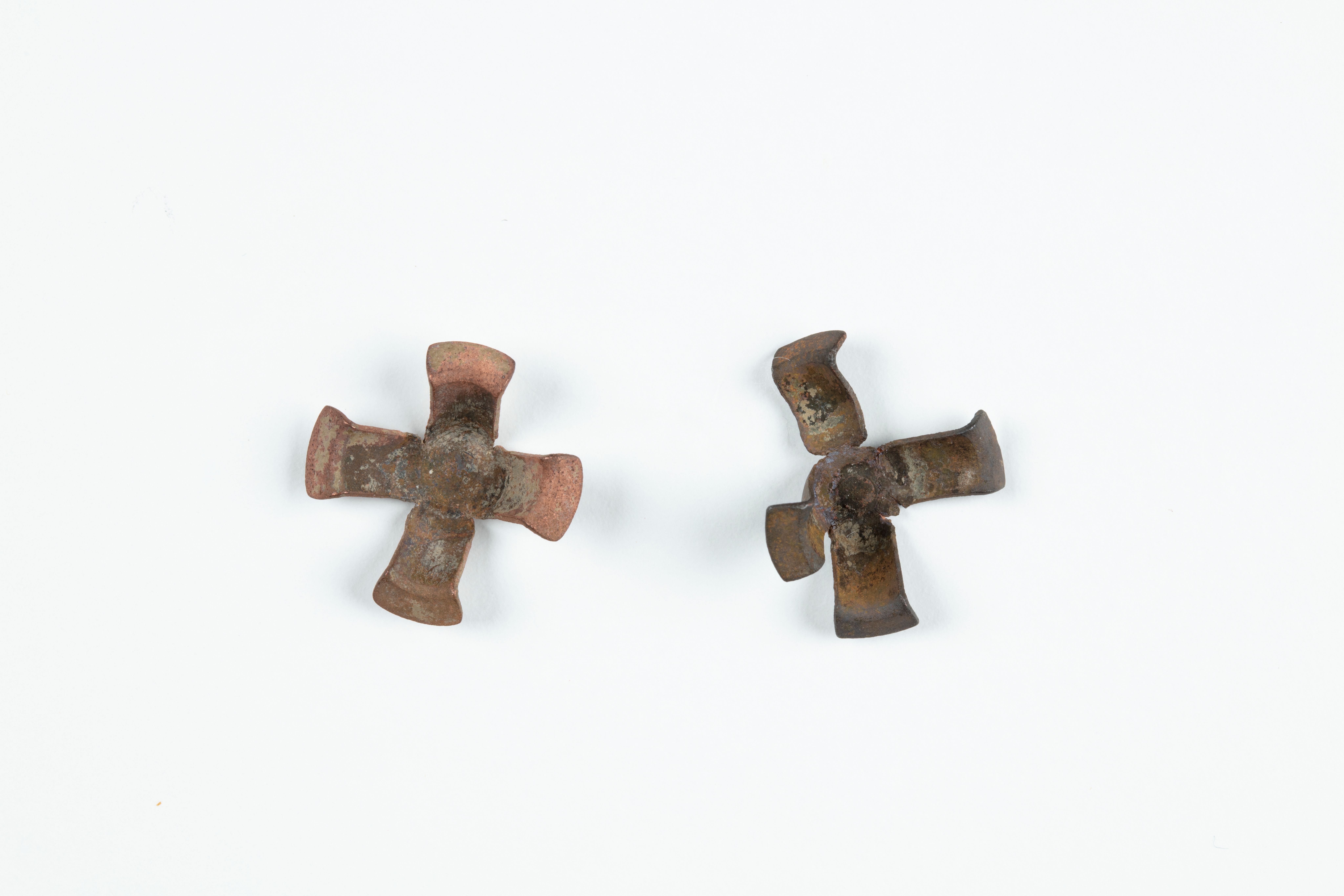 Two used brass percussion caps, each with four arms joined at centre with ends bent upwards. One is damaged, with one arm nearly detached. The other has marks of firing on the reverse.