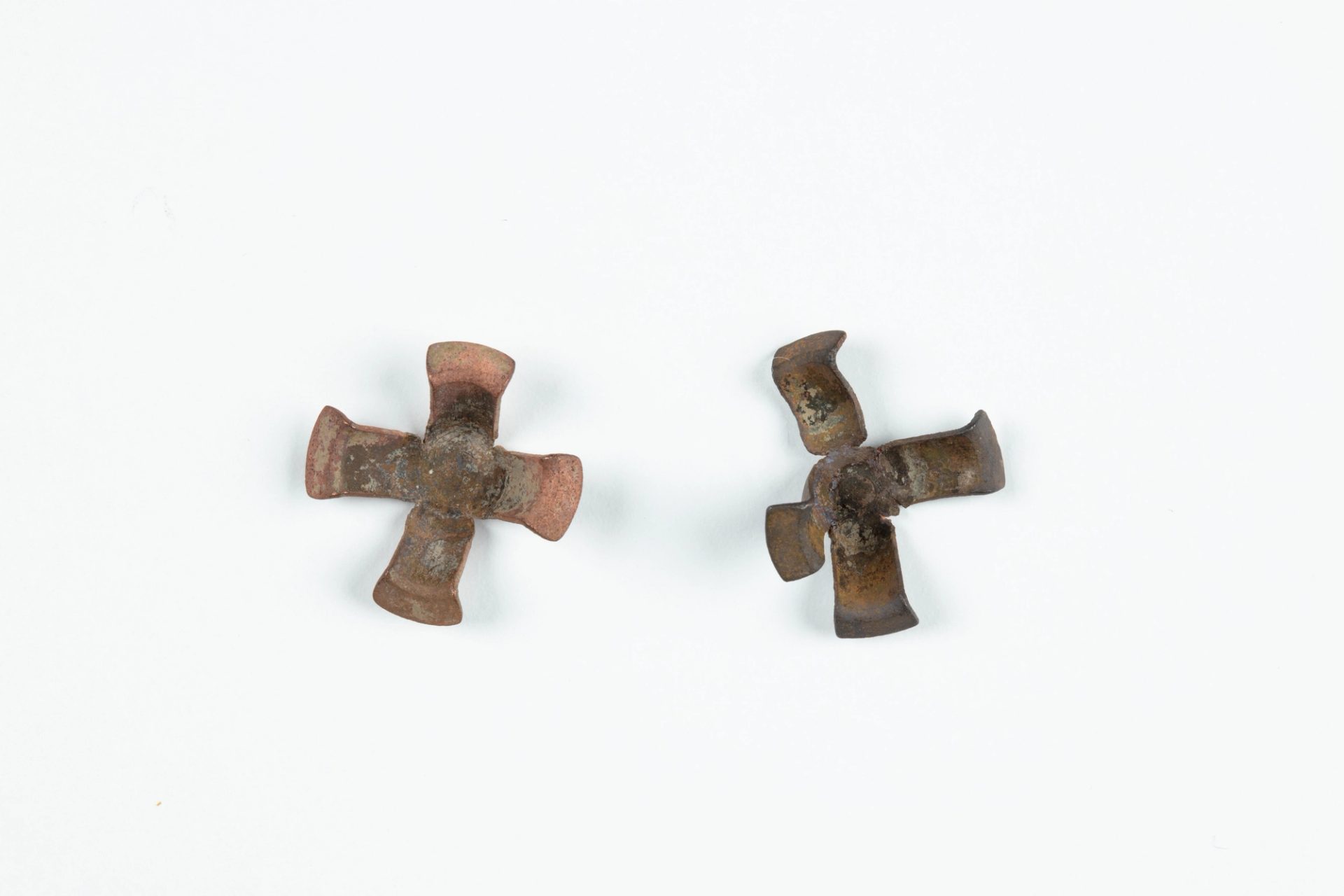 Two used brass percussion caps, each with four arms joined at centre with ends bent upwards. One is damaged, with one arm nearly detached. The other has marks of firing on the reverse.