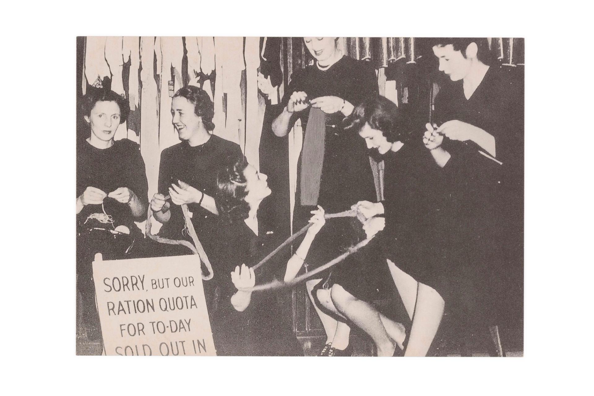 Six women in black work uniforms holding wool and knitting needles. A sign in the front left reads ‘SORRY, BUT OUR RATION QUOTA FOR TO-DAY SOLD OUT IN’