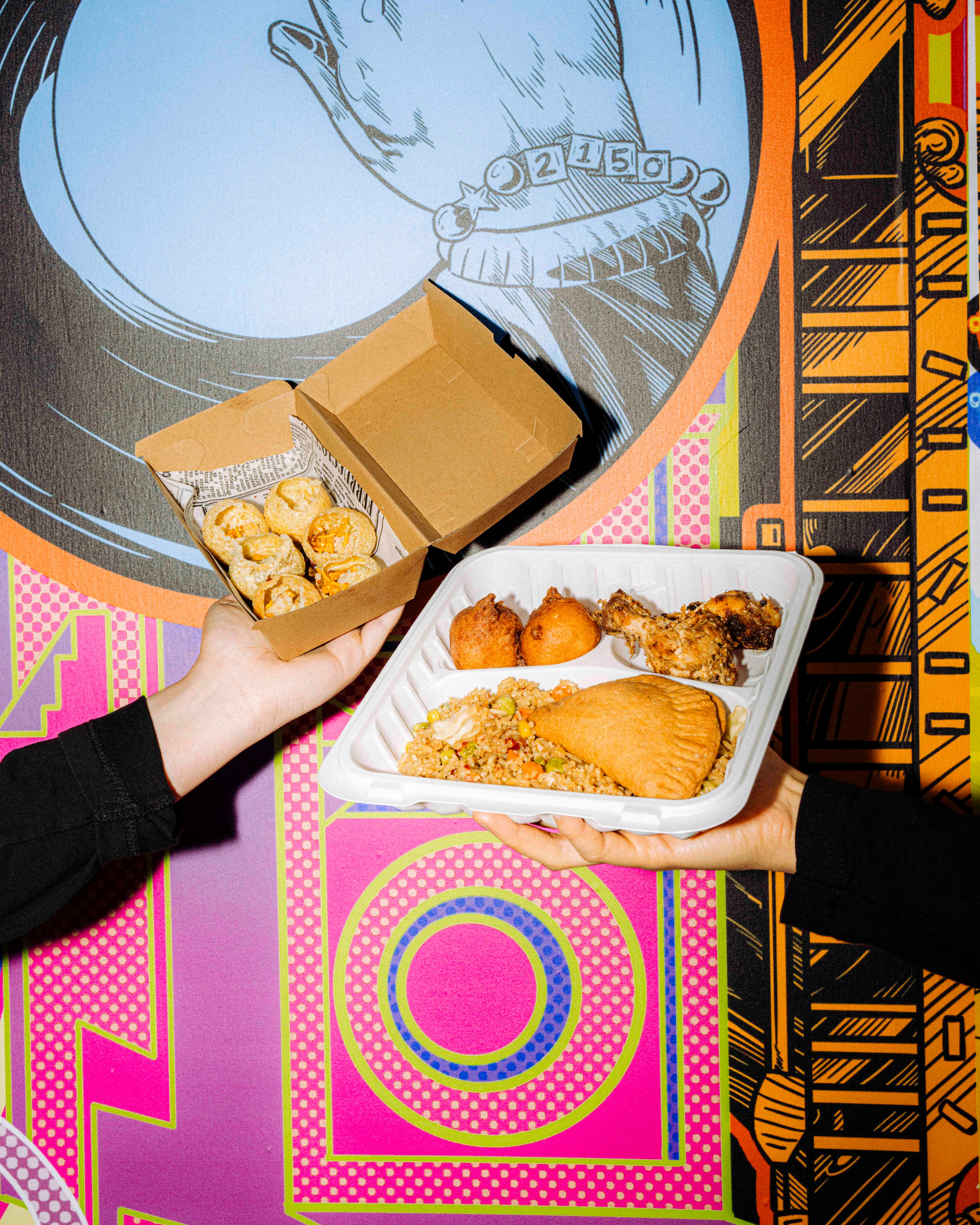 One hand holds up a cardboard box of golden round pieces of food; another lifts a white tray of assorted dishes, all set against a colourful mural backdrop.