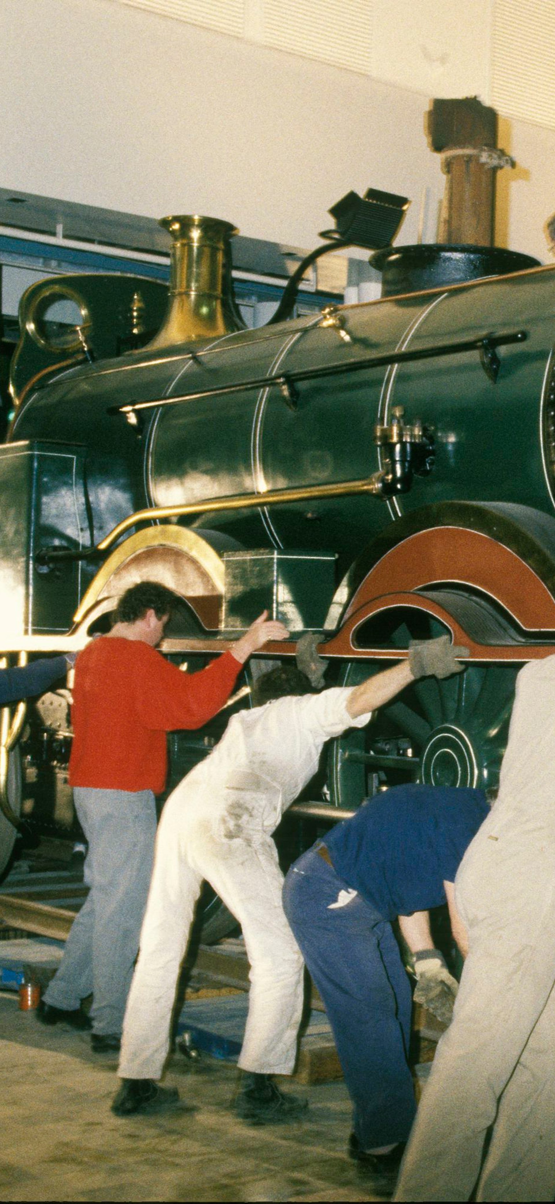 A group of workers surround the front engine of a steam train to pull and push it on a track into the museum.