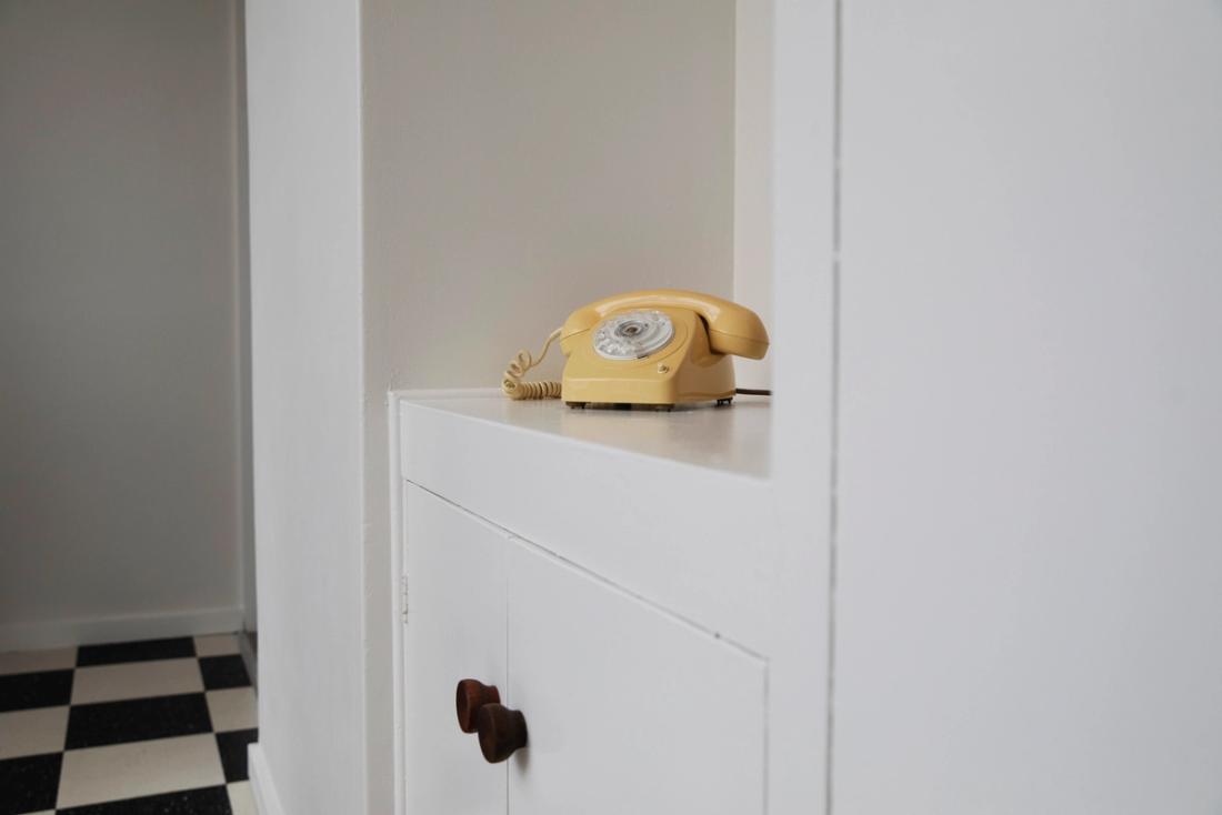 A yellow telephone sits on a white cabinet top
