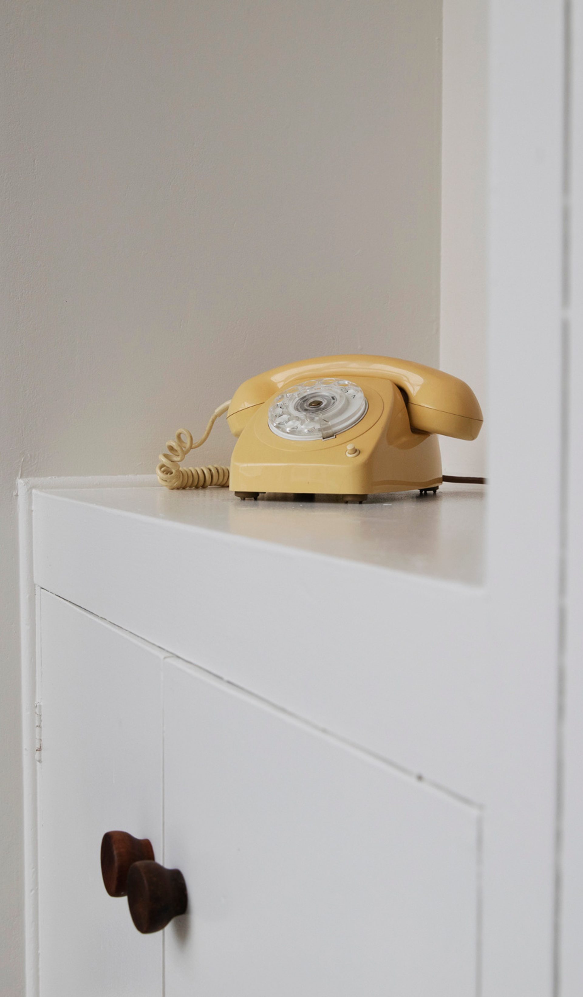 A yellow telephone sits on a white cabinet top