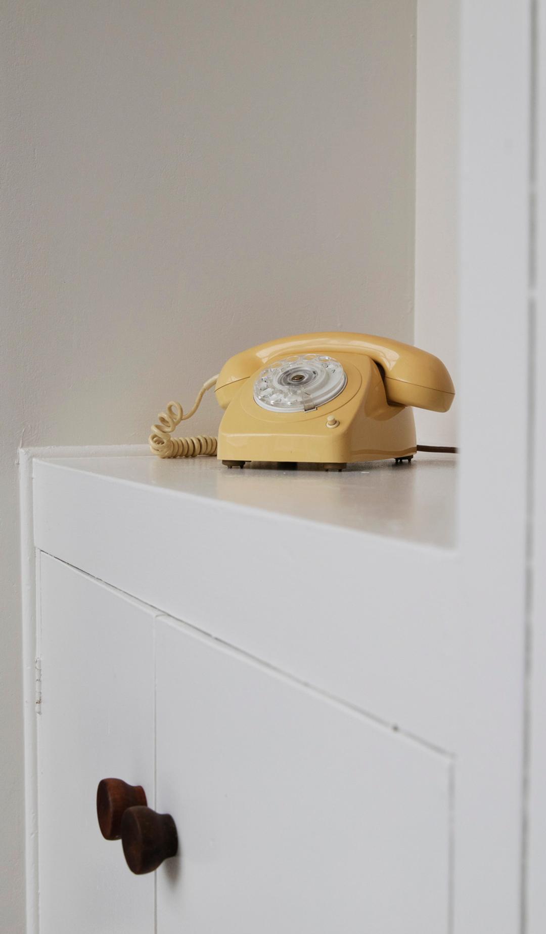 A yellow telephone sits on a white cabinet top