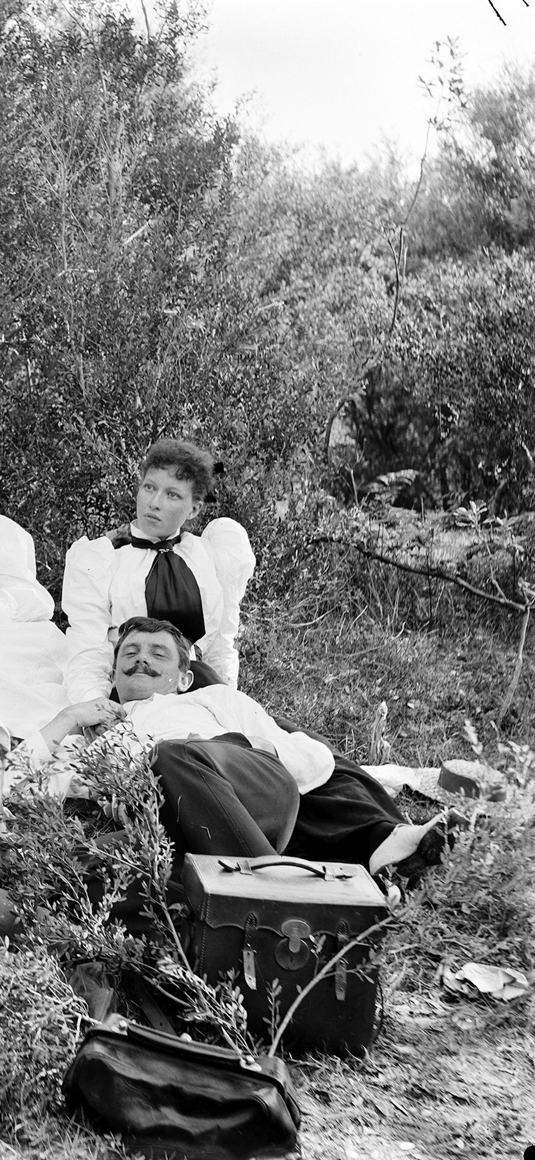 Landscape-format, black and white glass plate negative depicting a picnic scene at Freshwater, with young men and women and a small child