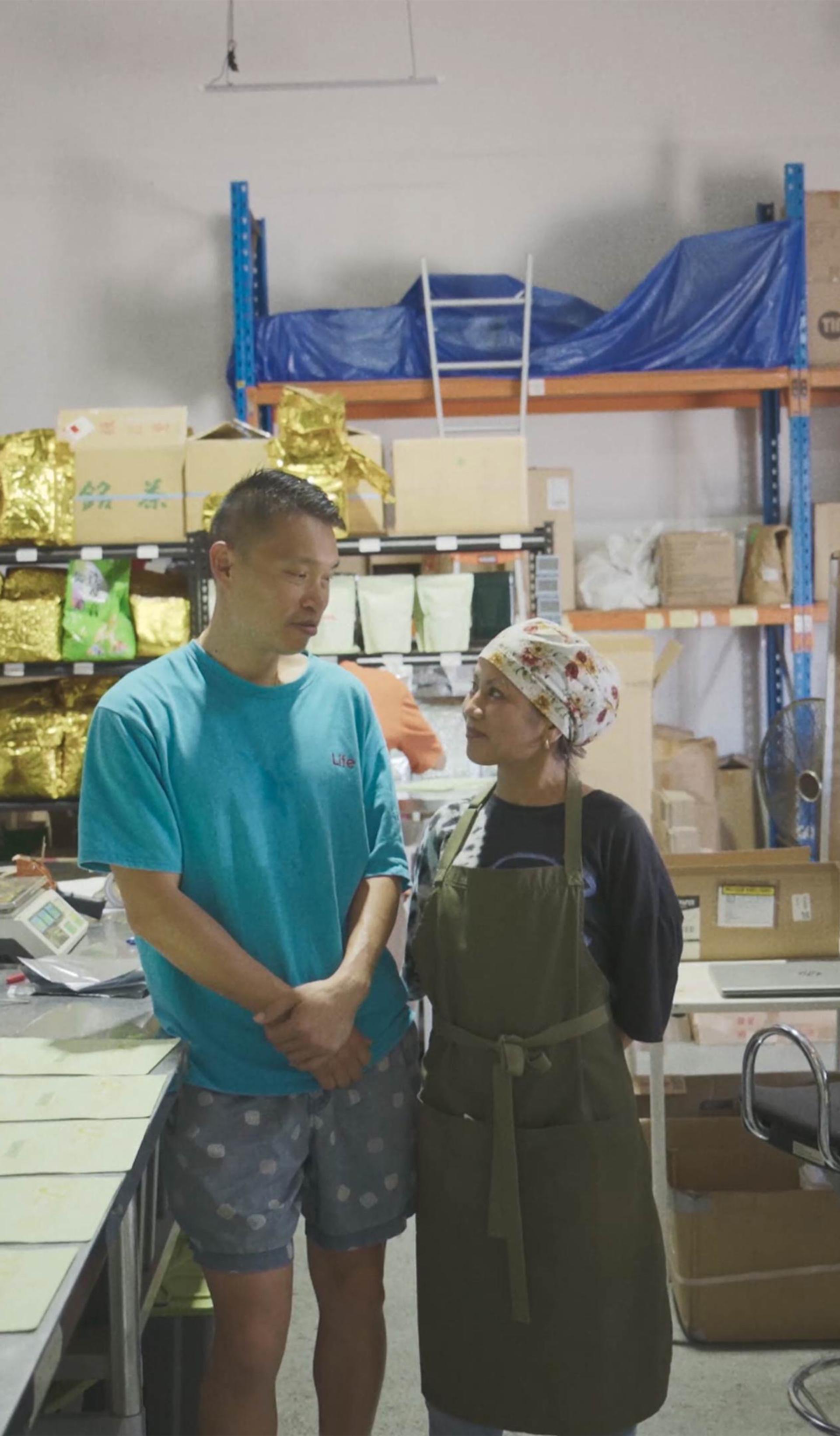 Two people standing in the middle of a tea manufactuing factory.