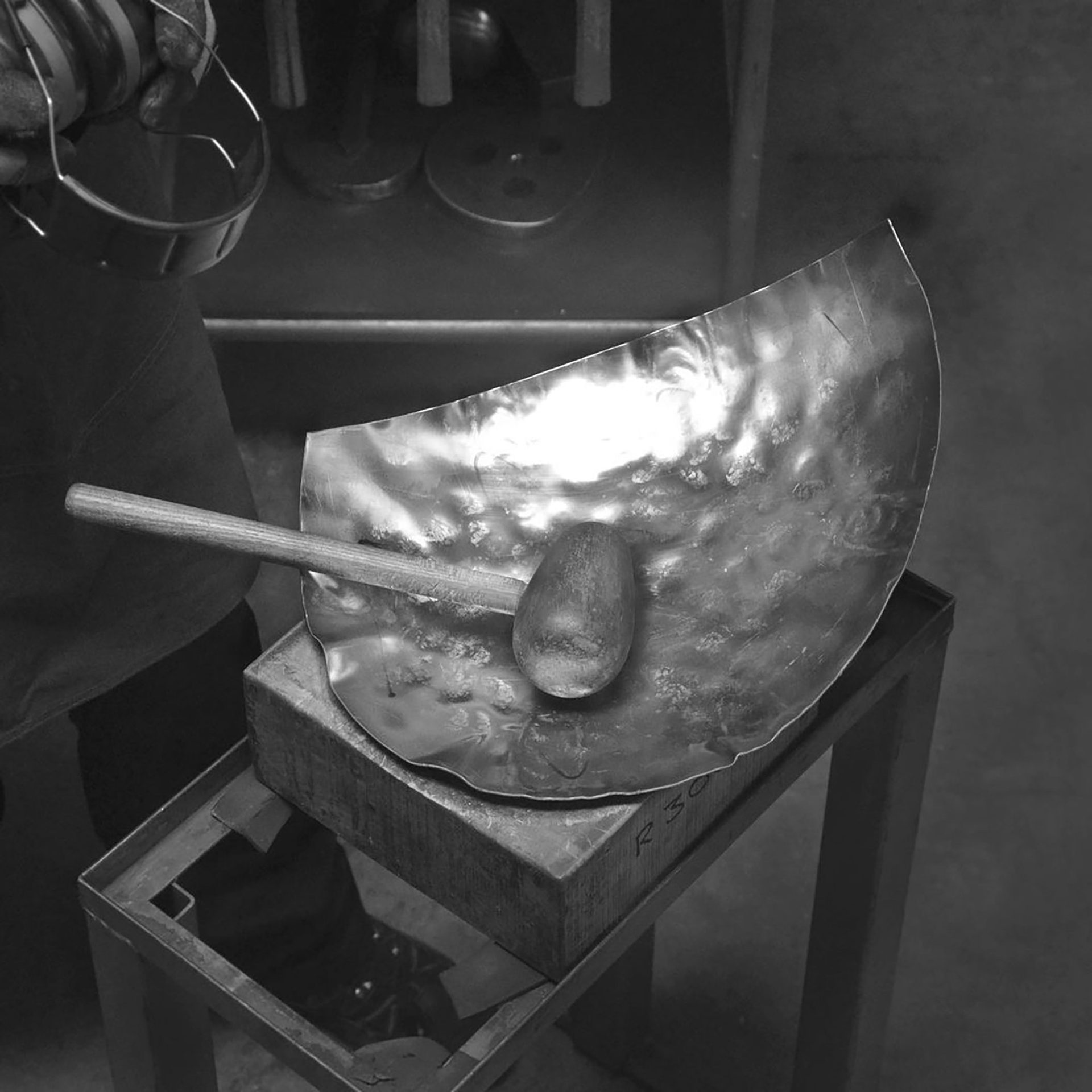 a section of a metal sphere on a work bench with a metal beater tool laying on top.