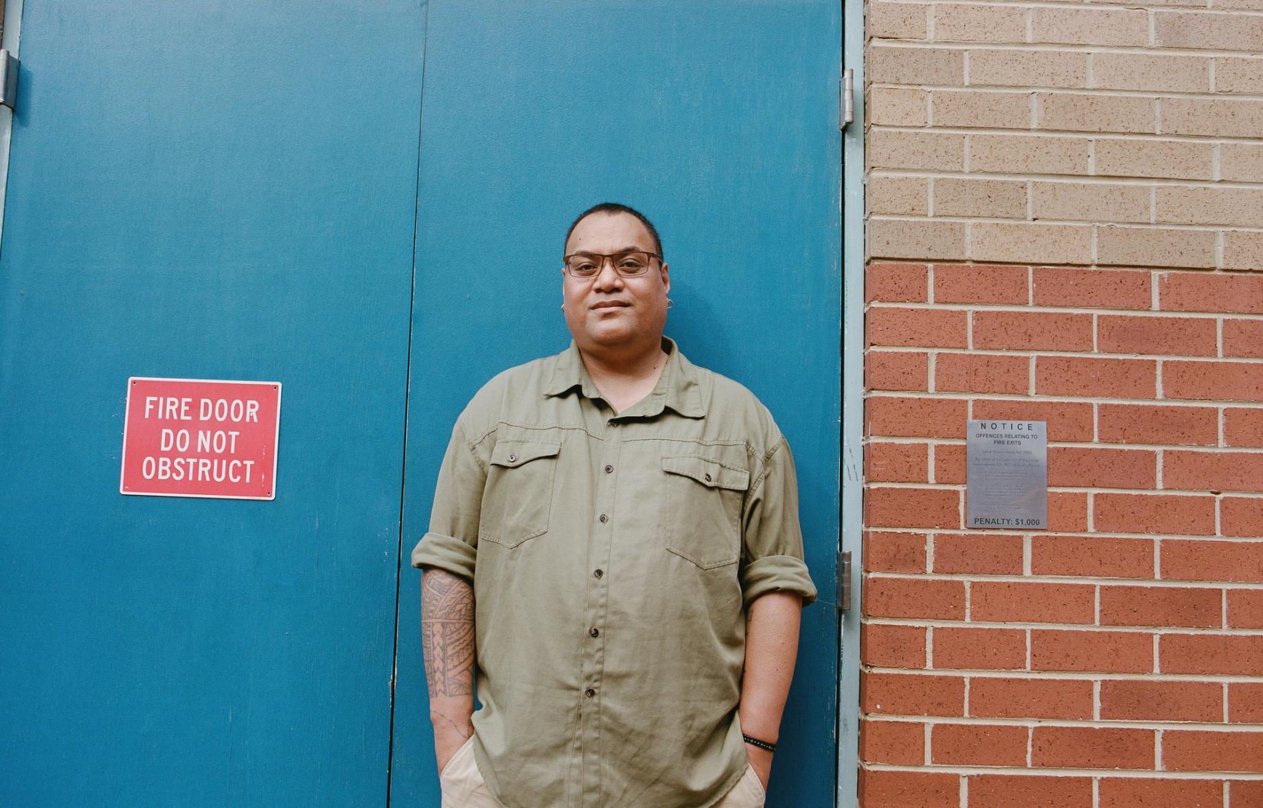 Person stand in front of a blue door, with their hands in their pocket.