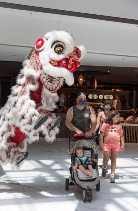 A Lunar New Year lion jumps next to a figure with a pram and two children.