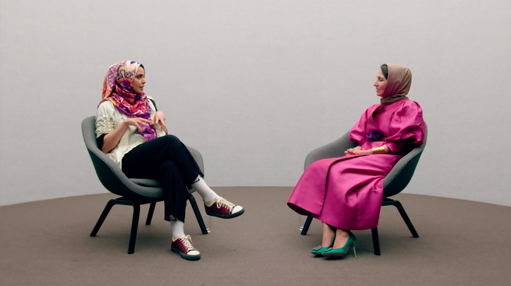 Two women sit on chairs talking to each other.
