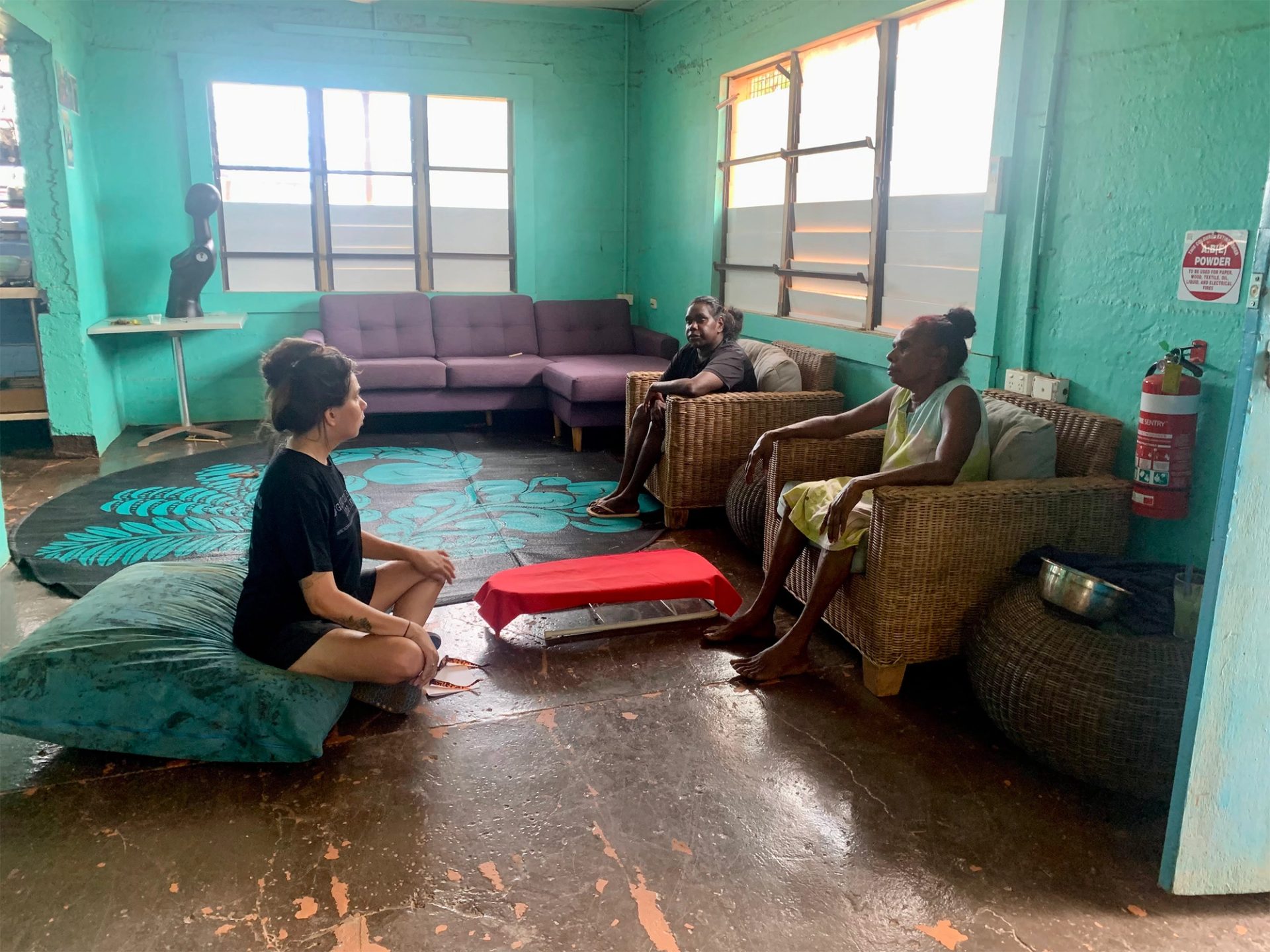 Three women sit talking in a room with aqua coloured walls.
