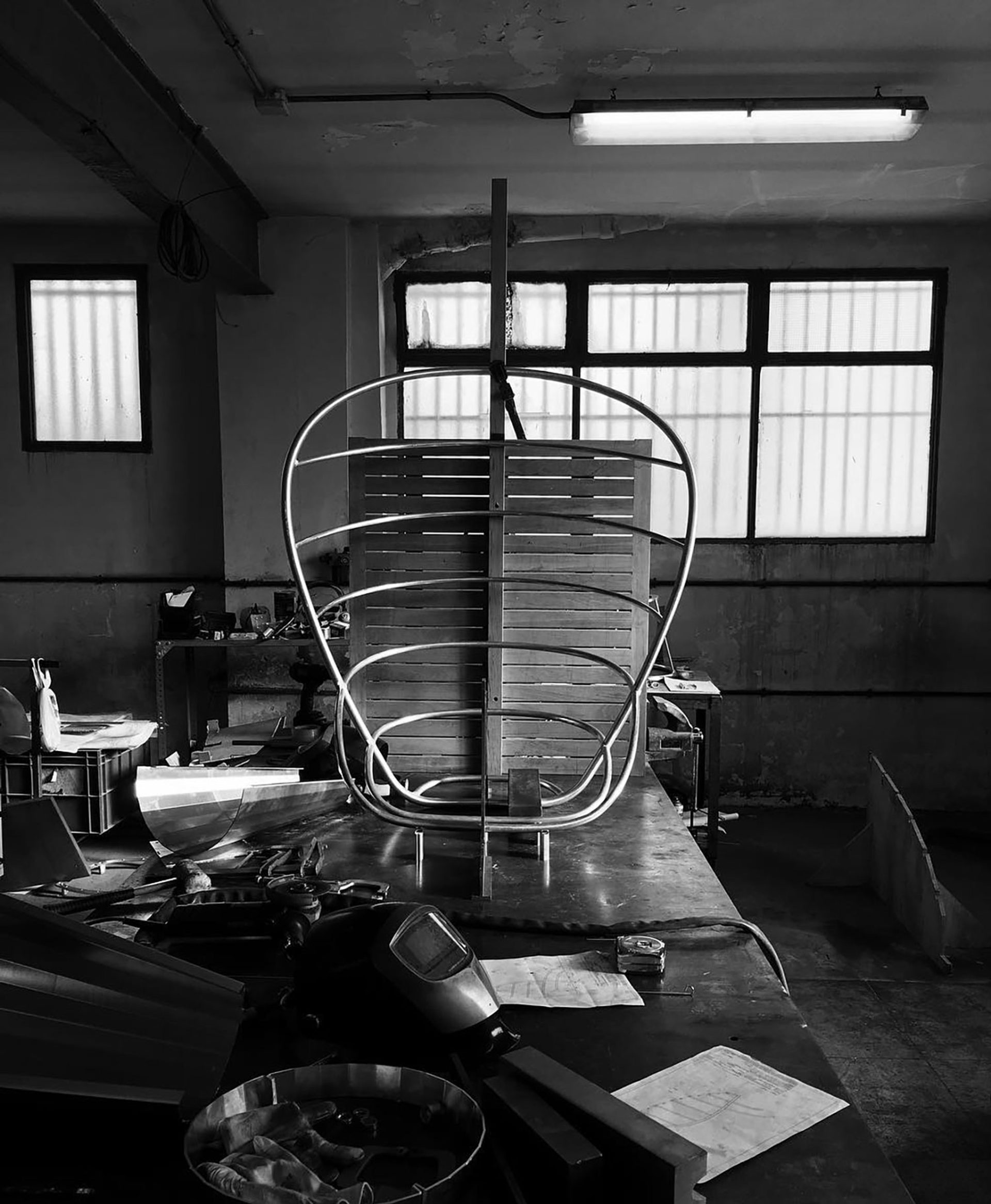 Black and white photograph of a metal curved structure with cross bars on top of a work table.