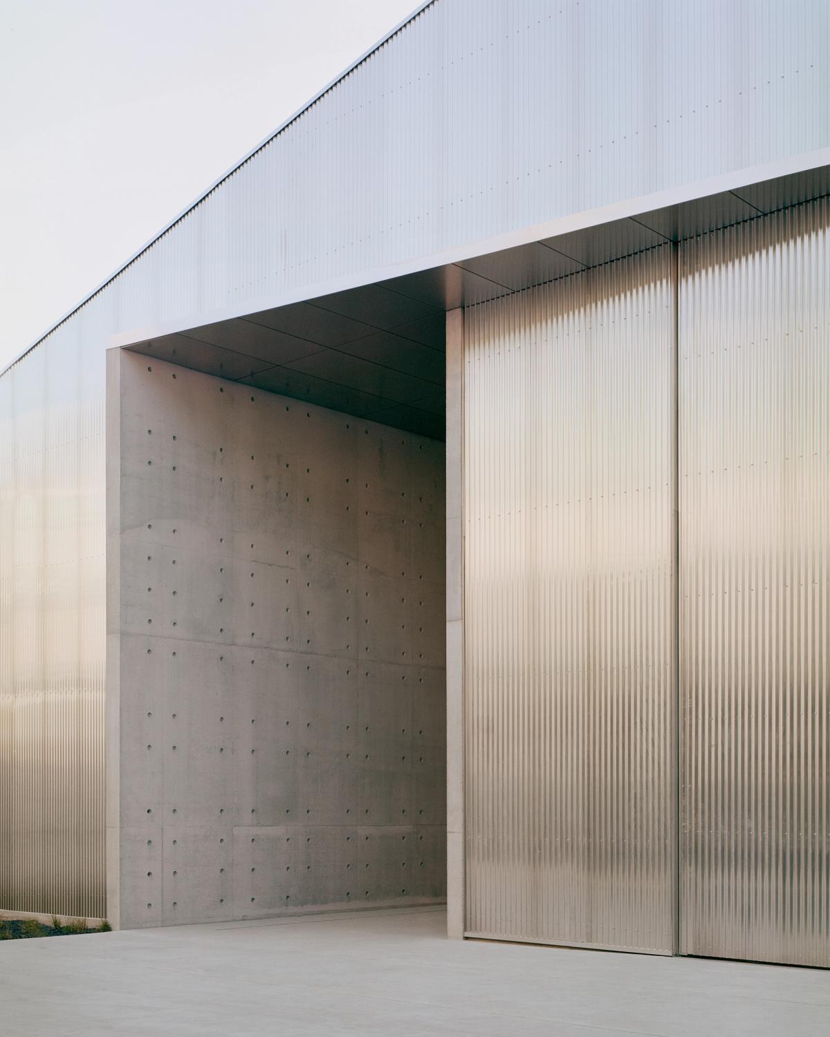 A two-storey entrance way made of concrete set into the side of a large building with an angled roof.