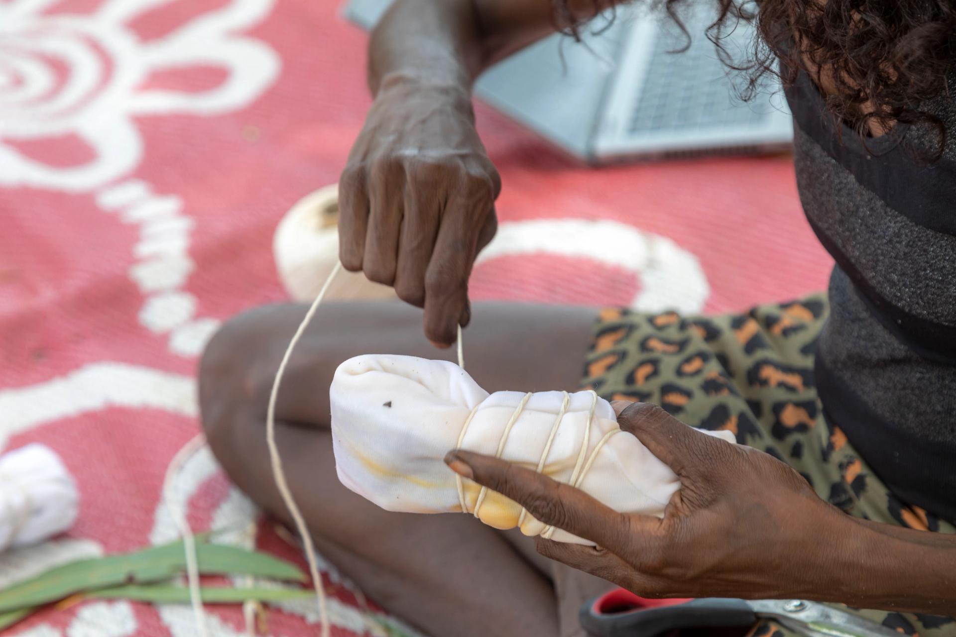 Two hands hold a bundle of white textile and are wrapping a piece of string around it.
