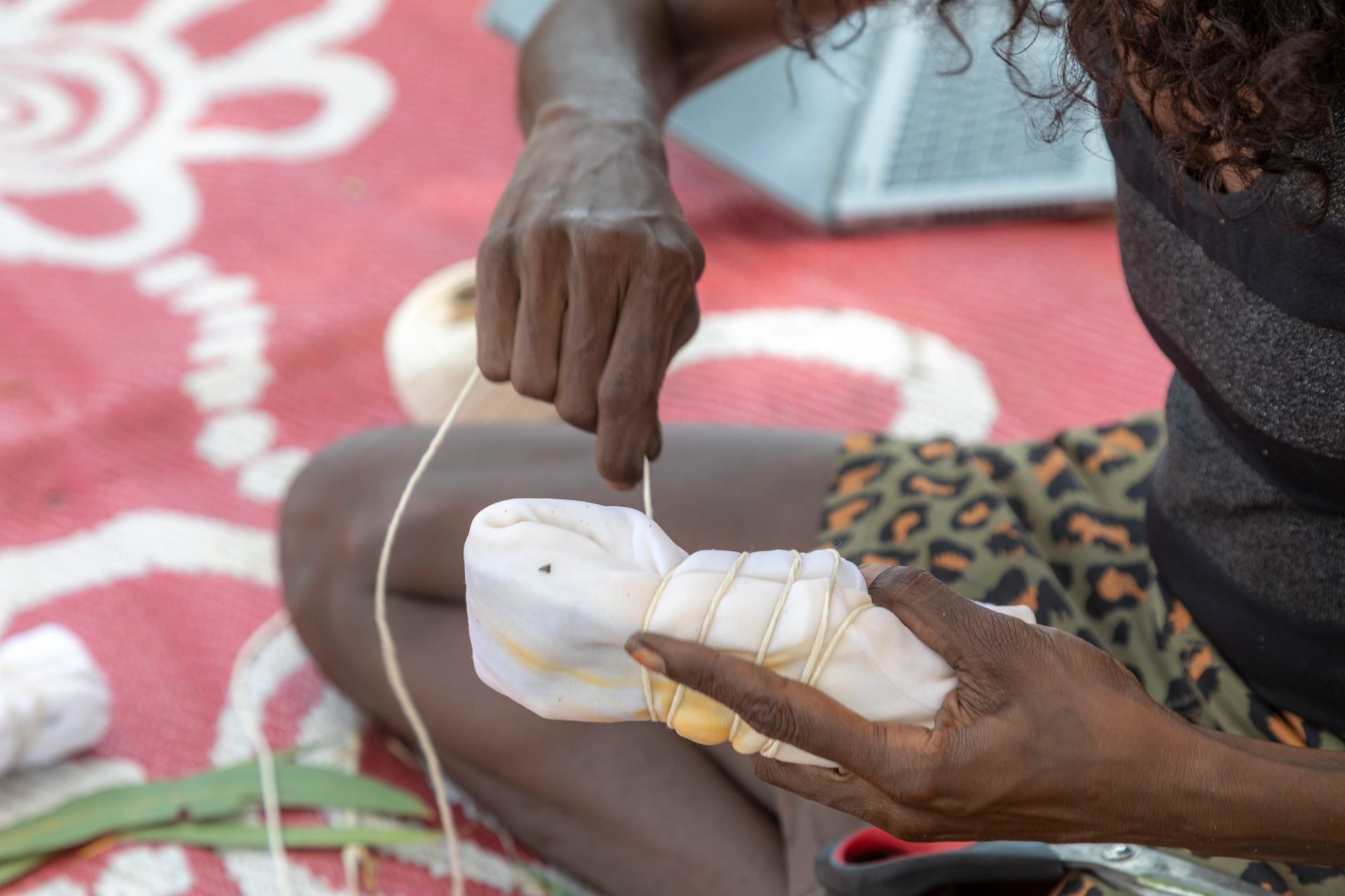 Two hands hold a bundle of white textile and are wrapping a piece of string around it.