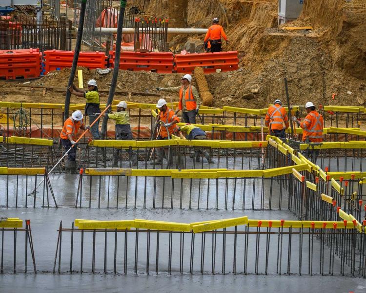 Construction workers in orange and yellow high-vis vests smooth out concrete.