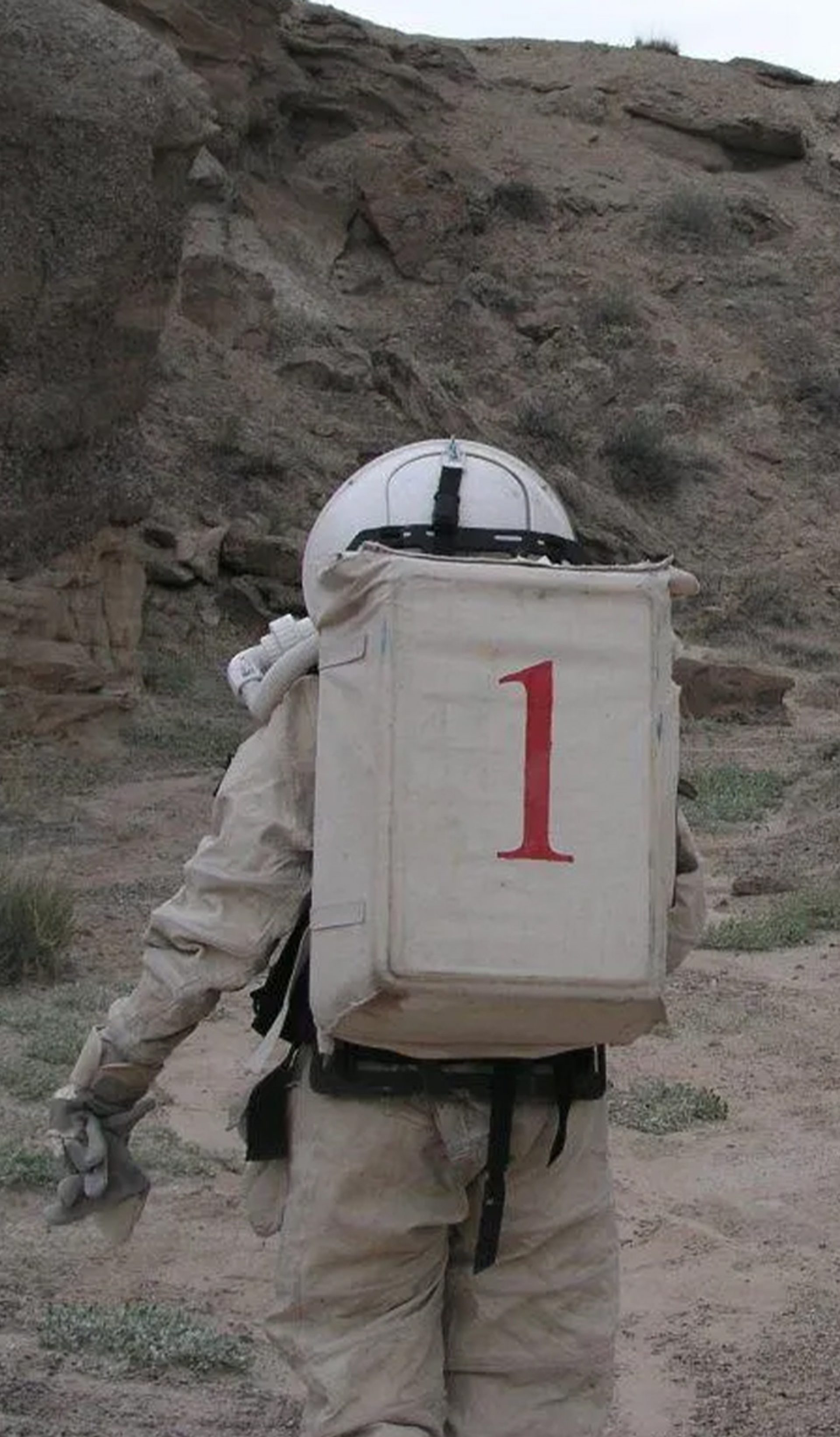 Two figures wearing space suits walk amongst a desert ranch.