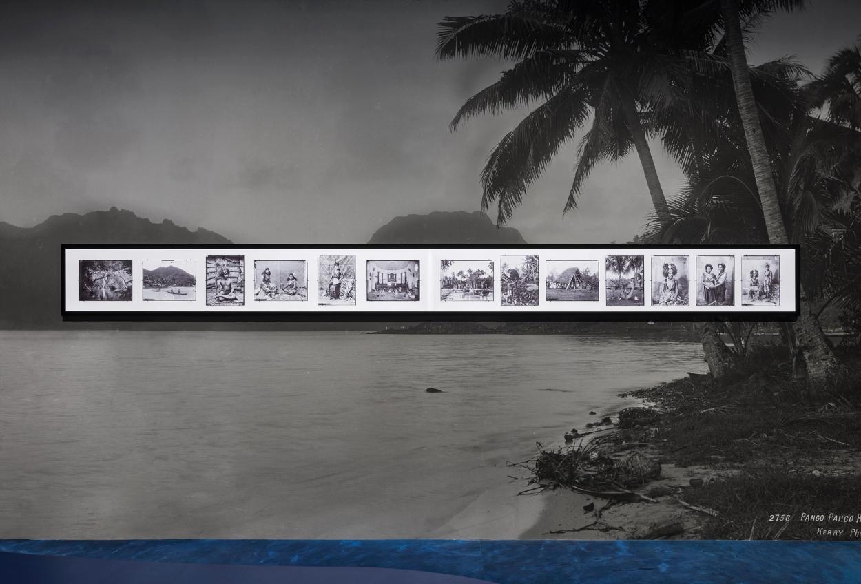 Thirteen glass plate images of Sāmoa and Sāmoan people mounted on a wall.