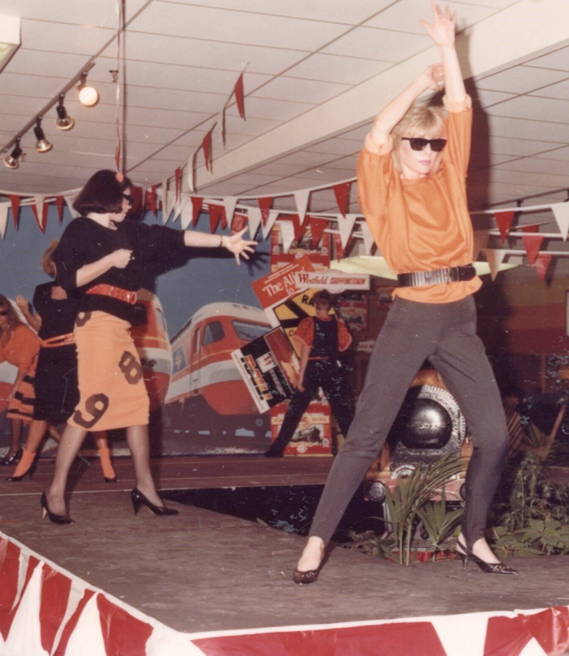 A photograph of women posing in black and orange clothes in a retail store, standing on a runway for the Hurstville Centenary Display.