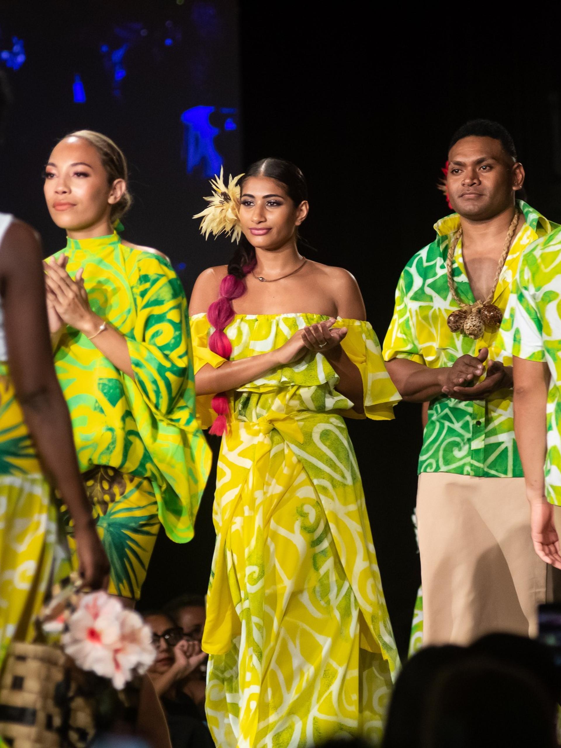 People walking down a runway clapping, wearing green flowy items.