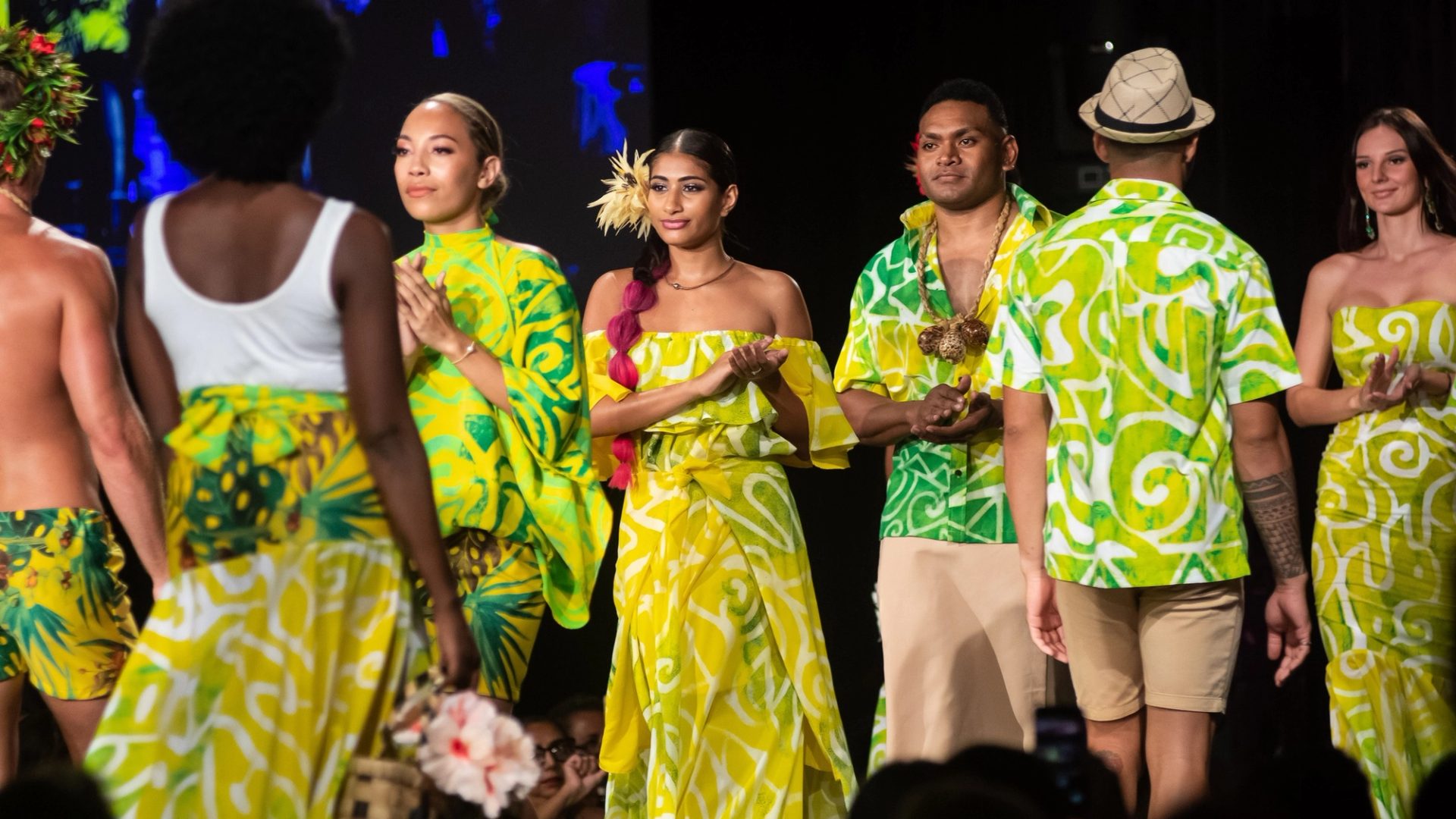 People walking down a runway clapping, wearing green flowy items.