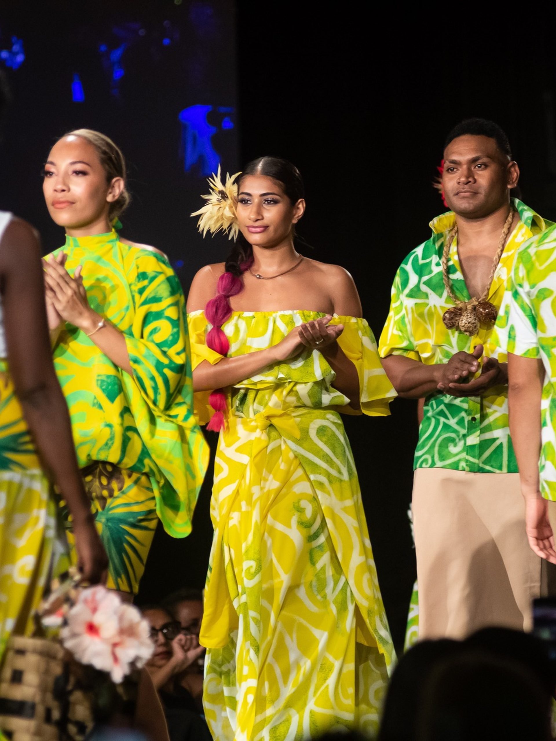 People walking down a runway clapping, wearing green flowy items.