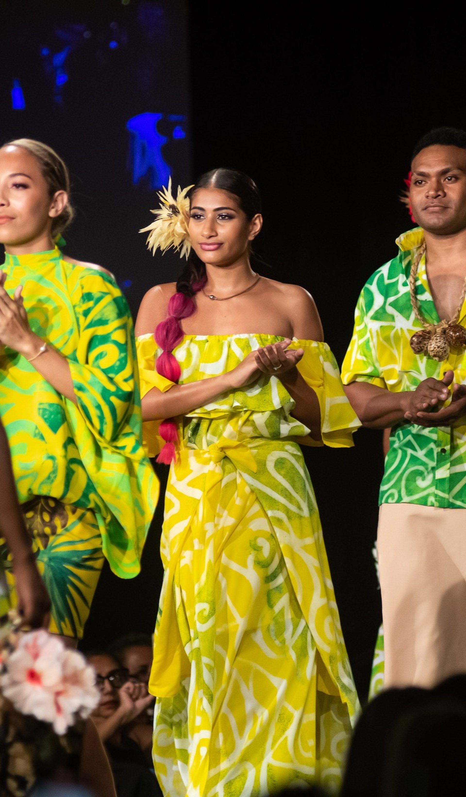 People walking down a runway clapping, wearing green flowy items.