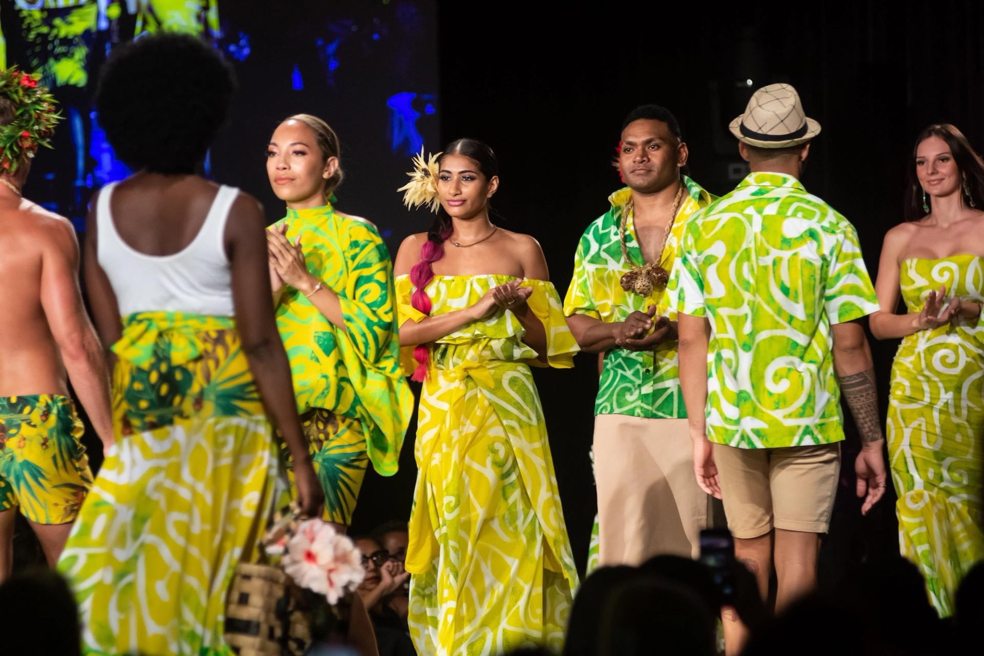 People walking down a runway clapping, wearing green flowy items.
