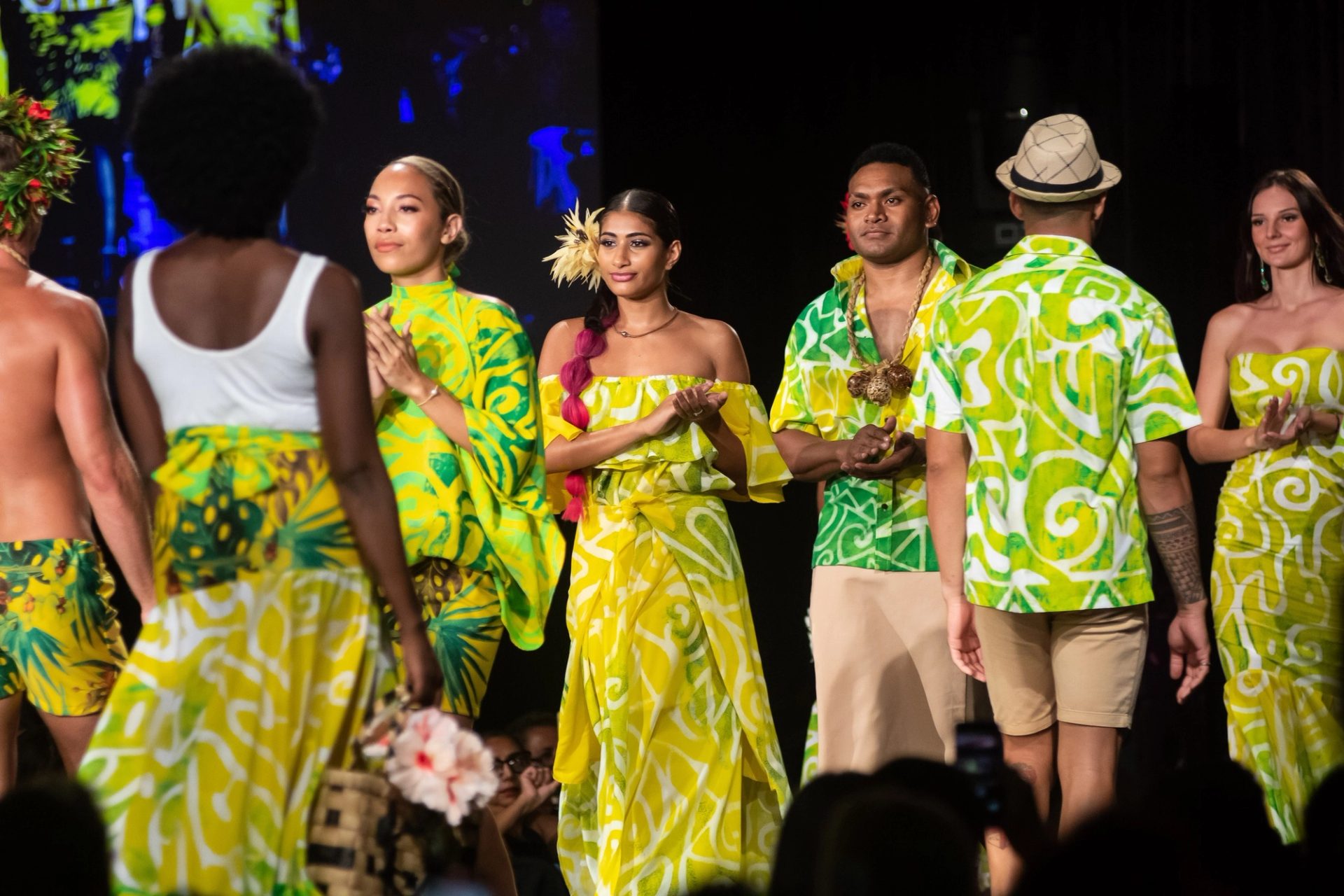 People walking down a runway clapping, wearing green flowy items.