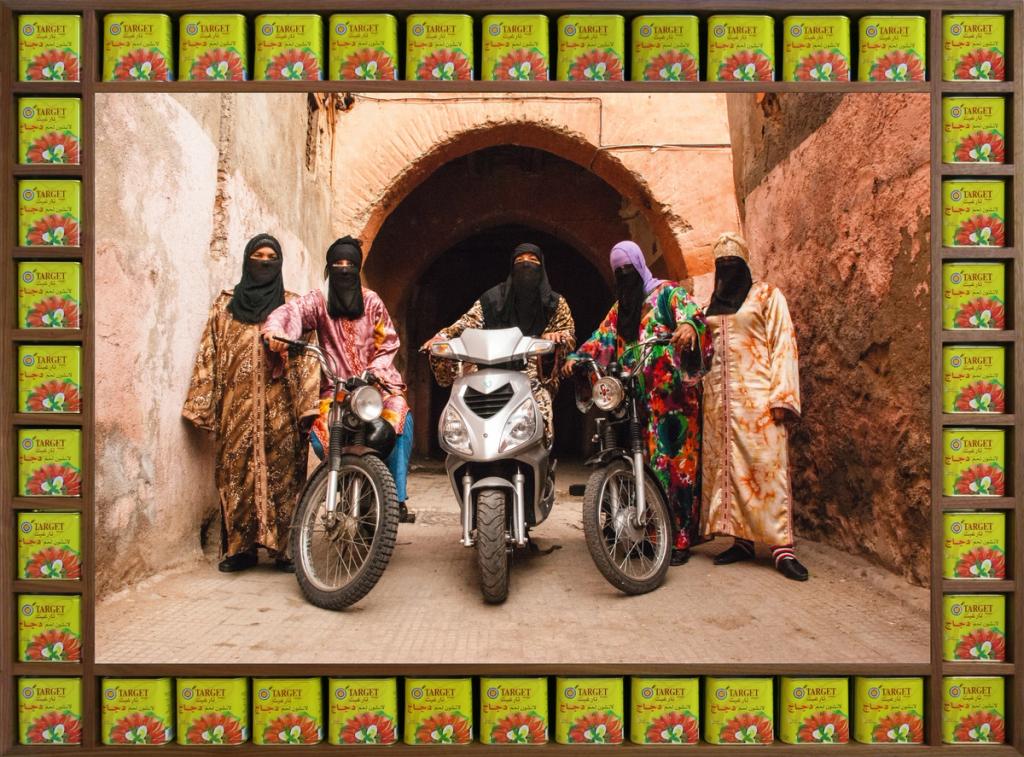 An art photograph that shows five figures in colourful Islamic-style dress with headscarves and black half niqabs. Three of the figures are astride motorcycles.