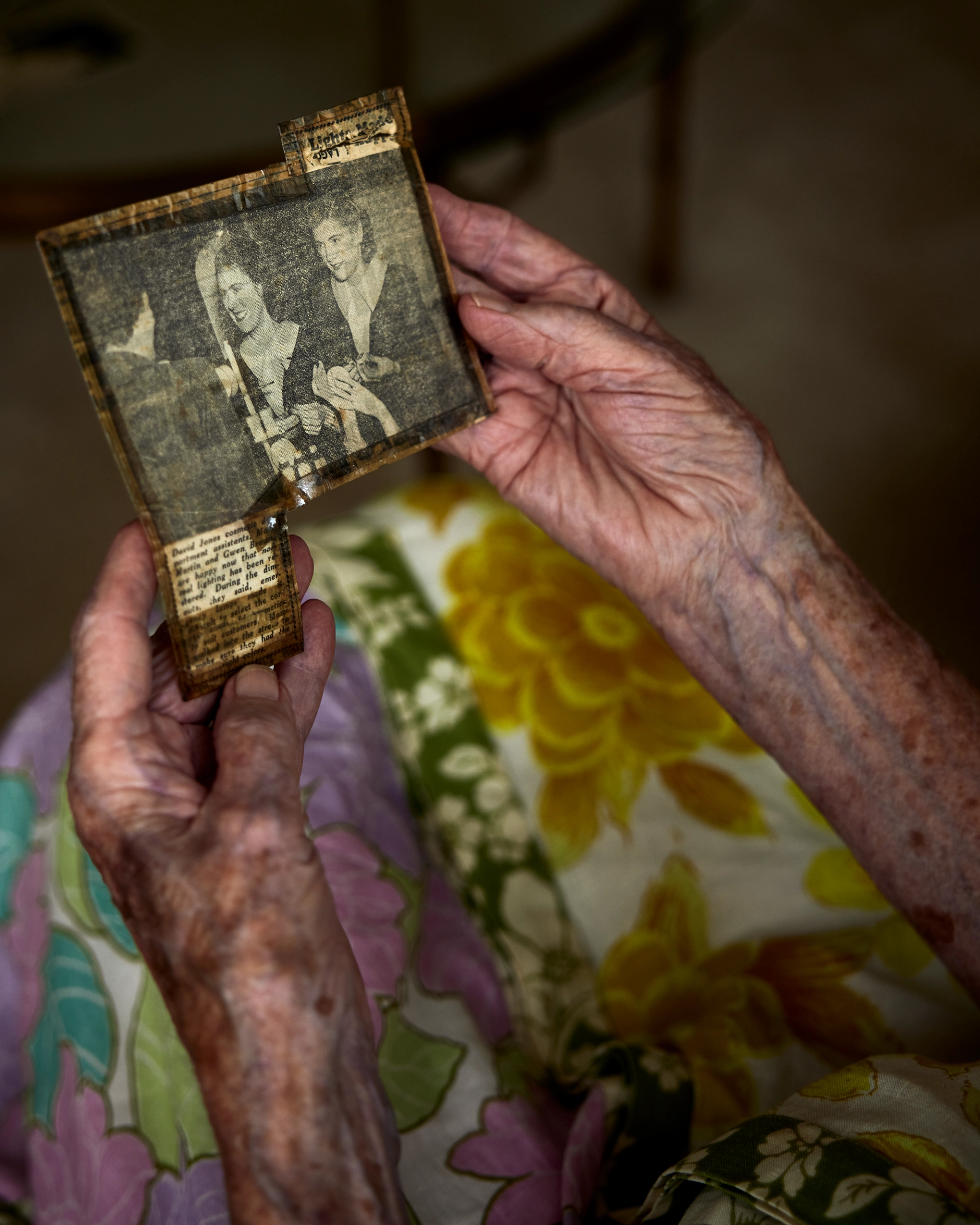 An elderly woman’s hands holding a 1949 newspaper article clipping.