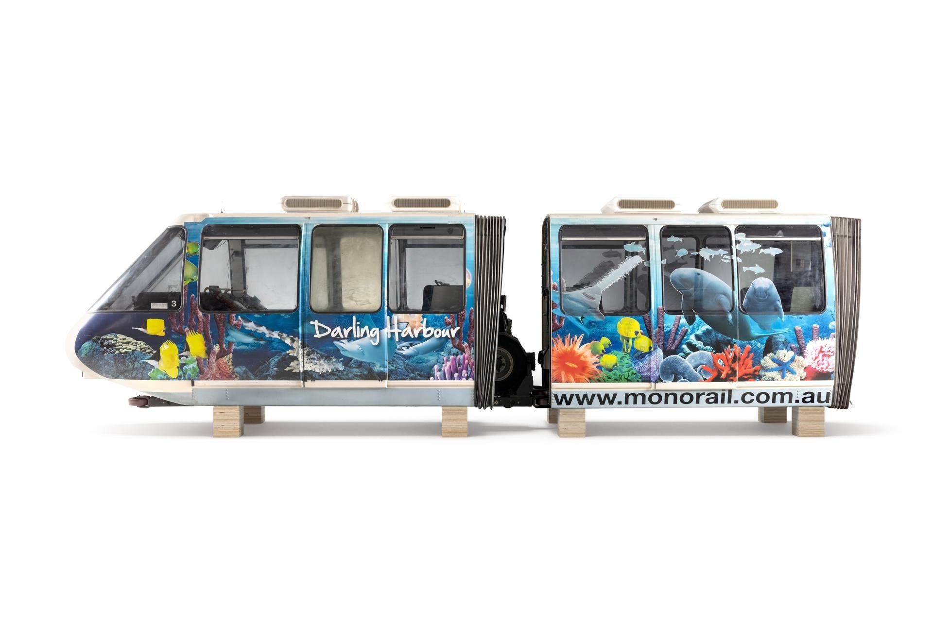 Side view of two monorail cars on wooden blocks. The outside panels include images of sea life such as star fish and text: 'Darling Harbour' and 'www.monorail.com.au'