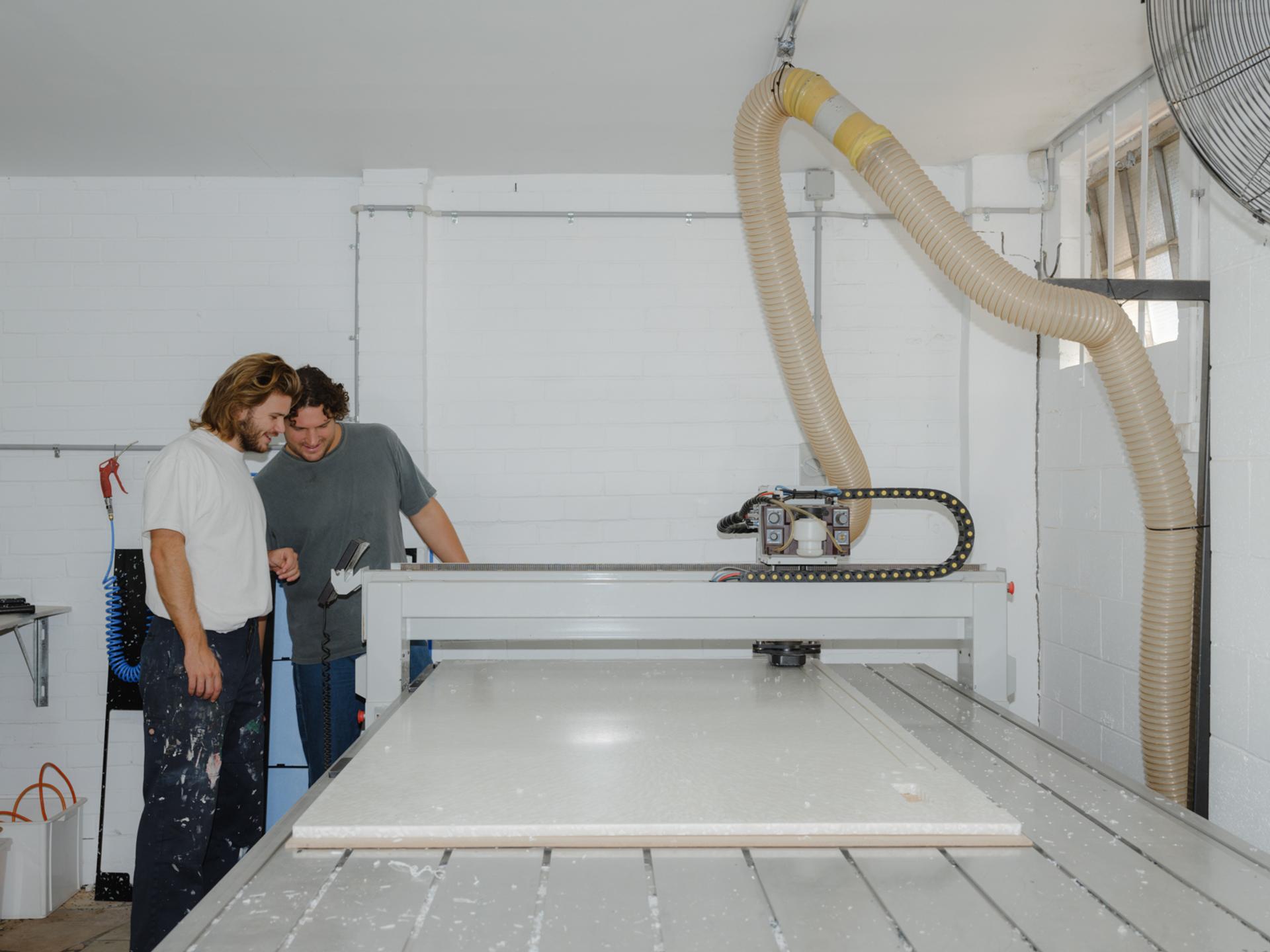Two figures looking at the cutting of a large piece of plastic.