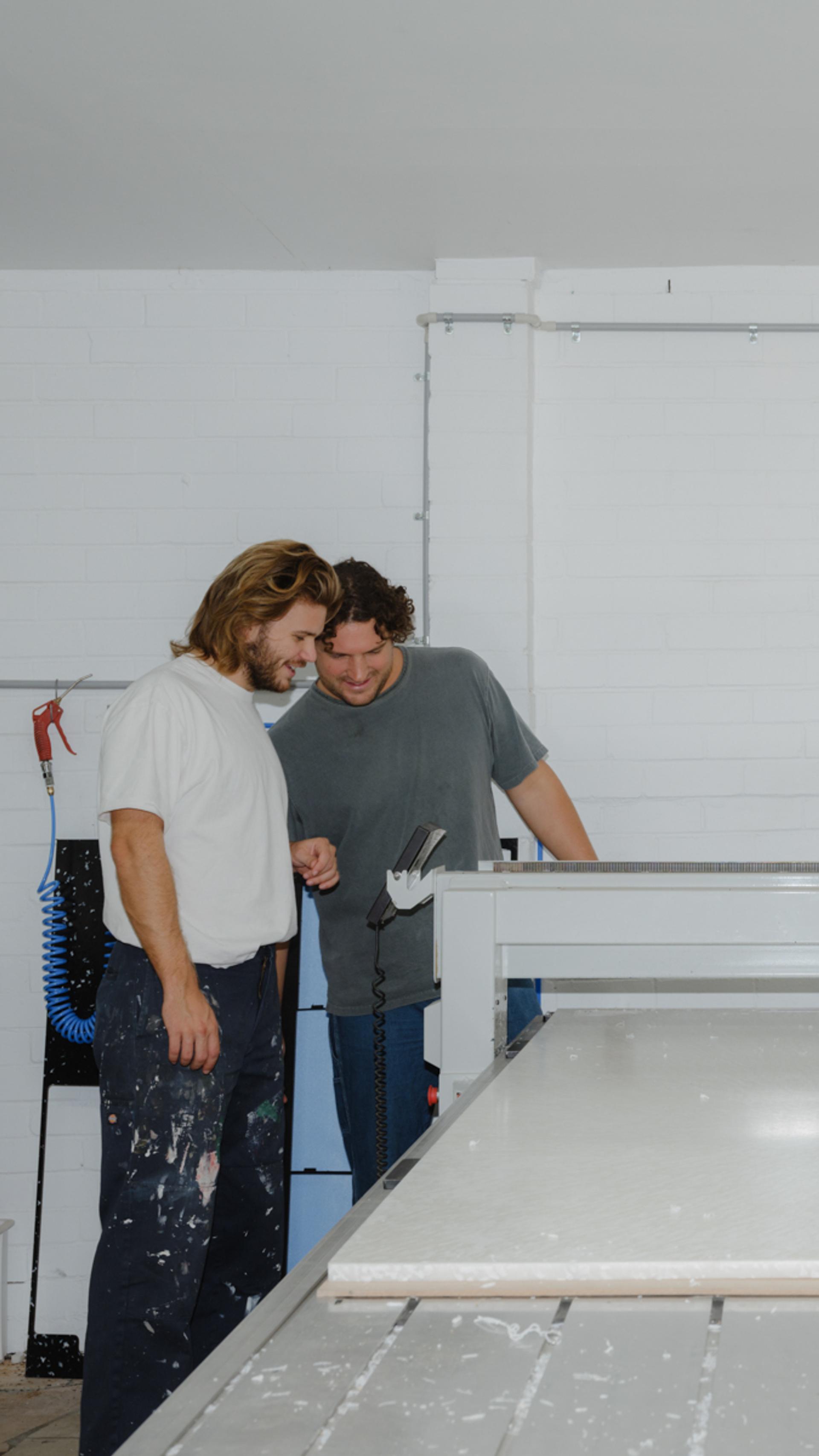 Two figures looking at the cutting of a large piece of plastic.