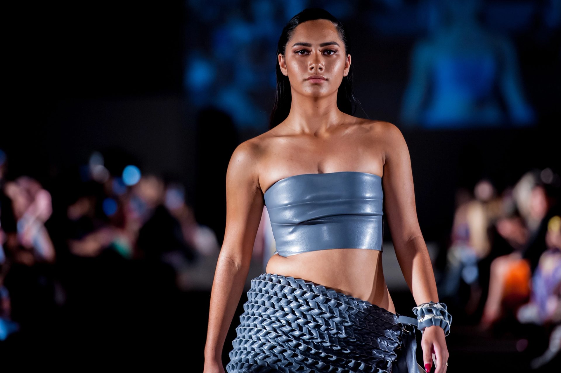 Woman walk catwalk wearing leathery weaving skirt and bandeau.