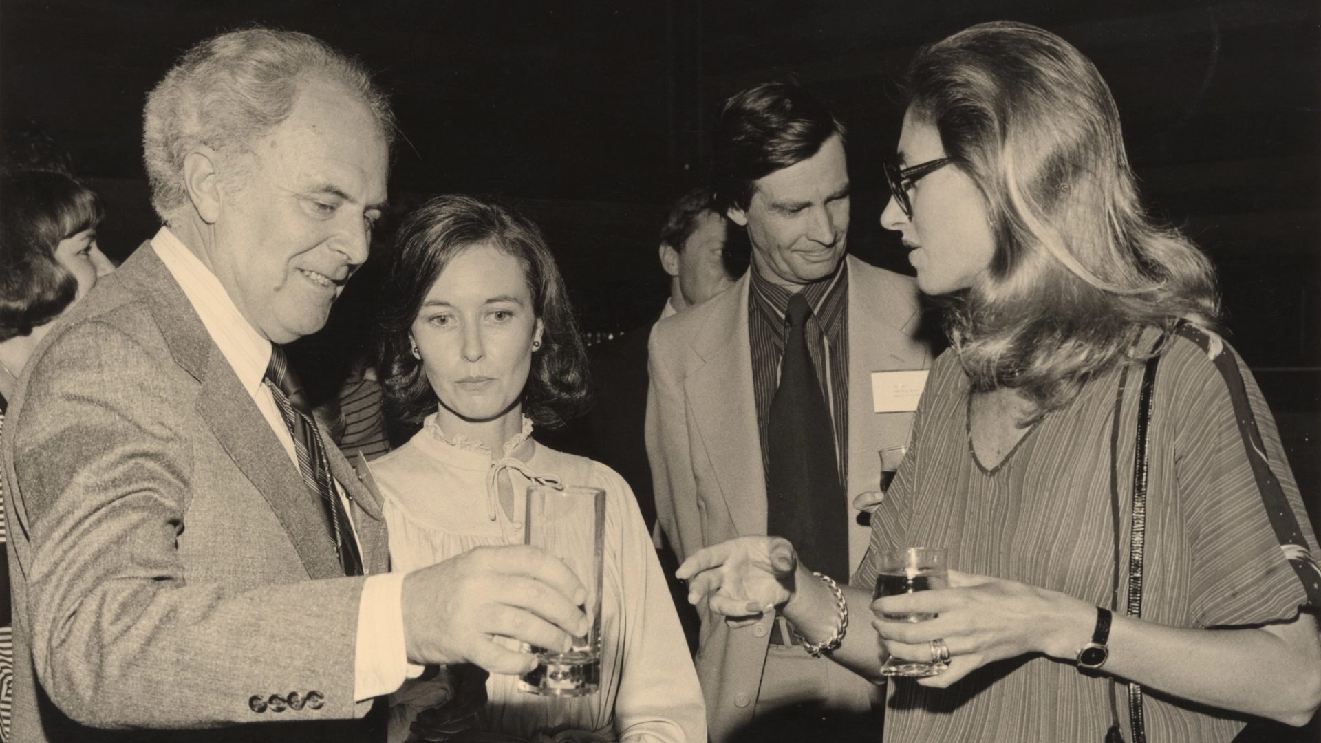 A sepia-toned photograph of the design awards, in which four figures -- two men, two women -- speak together in a loose huddle, drinks in hand.
