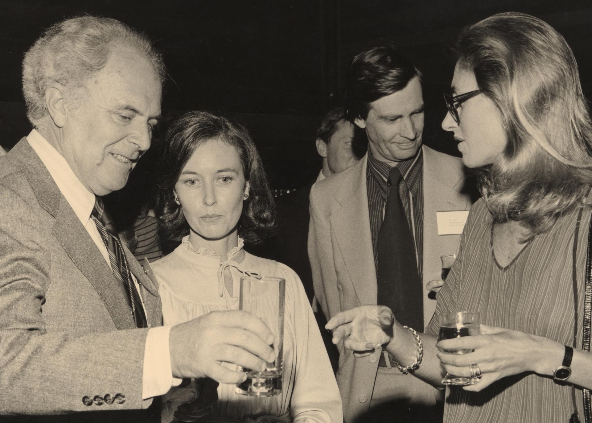 A sepia-toned photograph of the design awards, in which four figures -- two men, two women -- speak together in a loose huddle, drinks in hand.