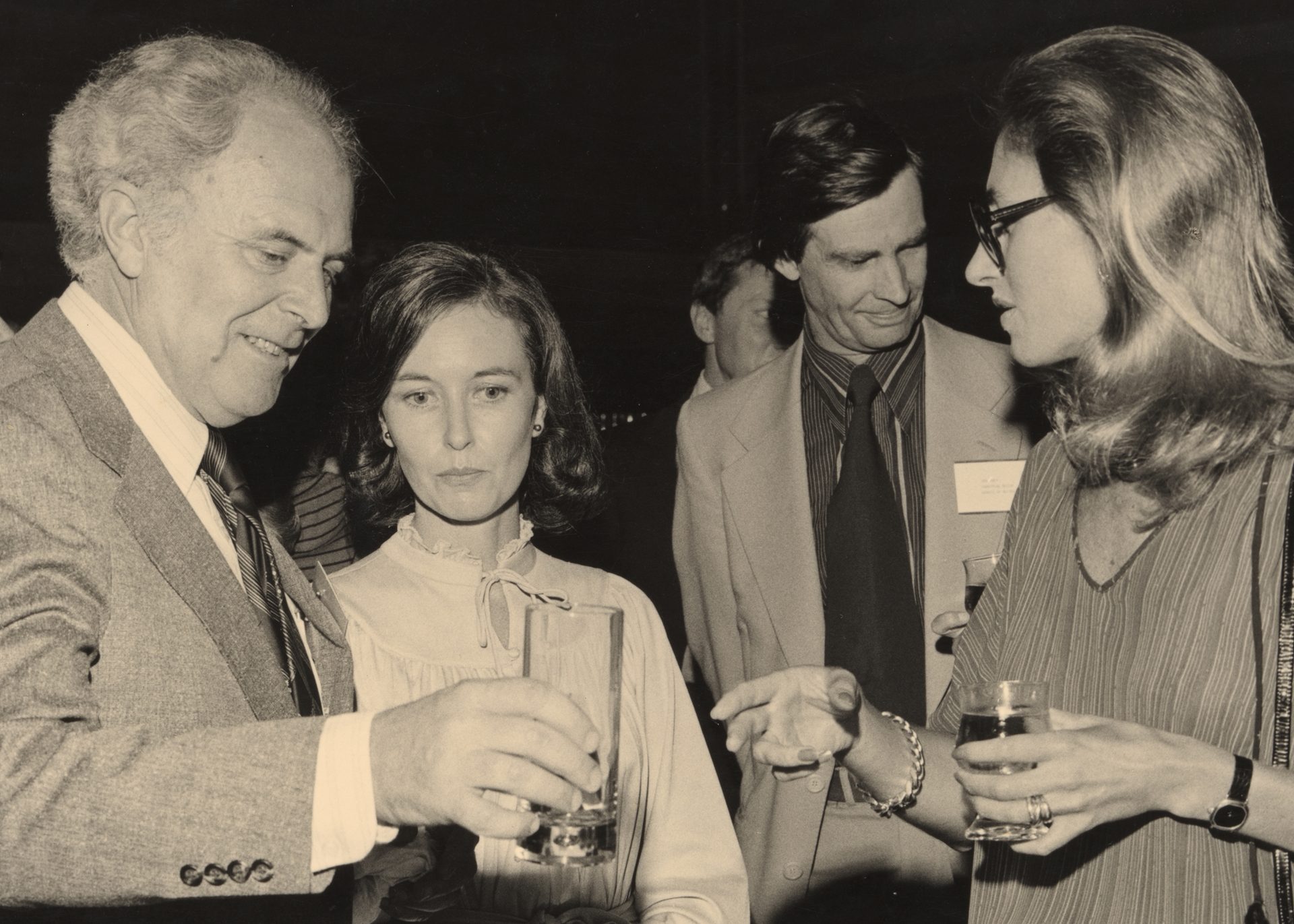 A sepia-toned photograph of the design awards, in which four figures -- two men, two women -- speak together in a loose huddle, drinks in hand.