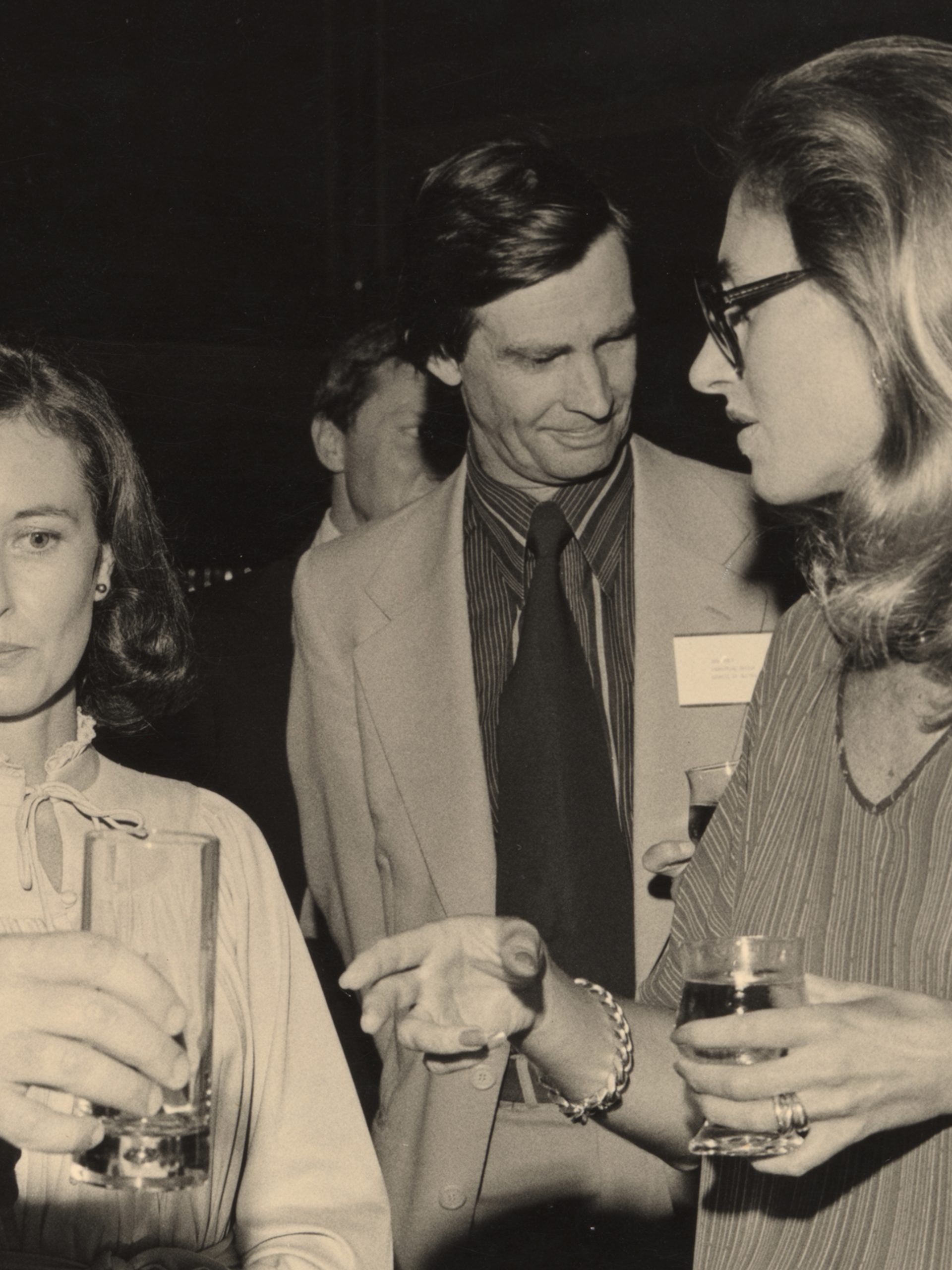 A sepia-toned photograph of the design awards, in which four figures -- two men, two women -- speak together in a loose huddle, drinks in hand.