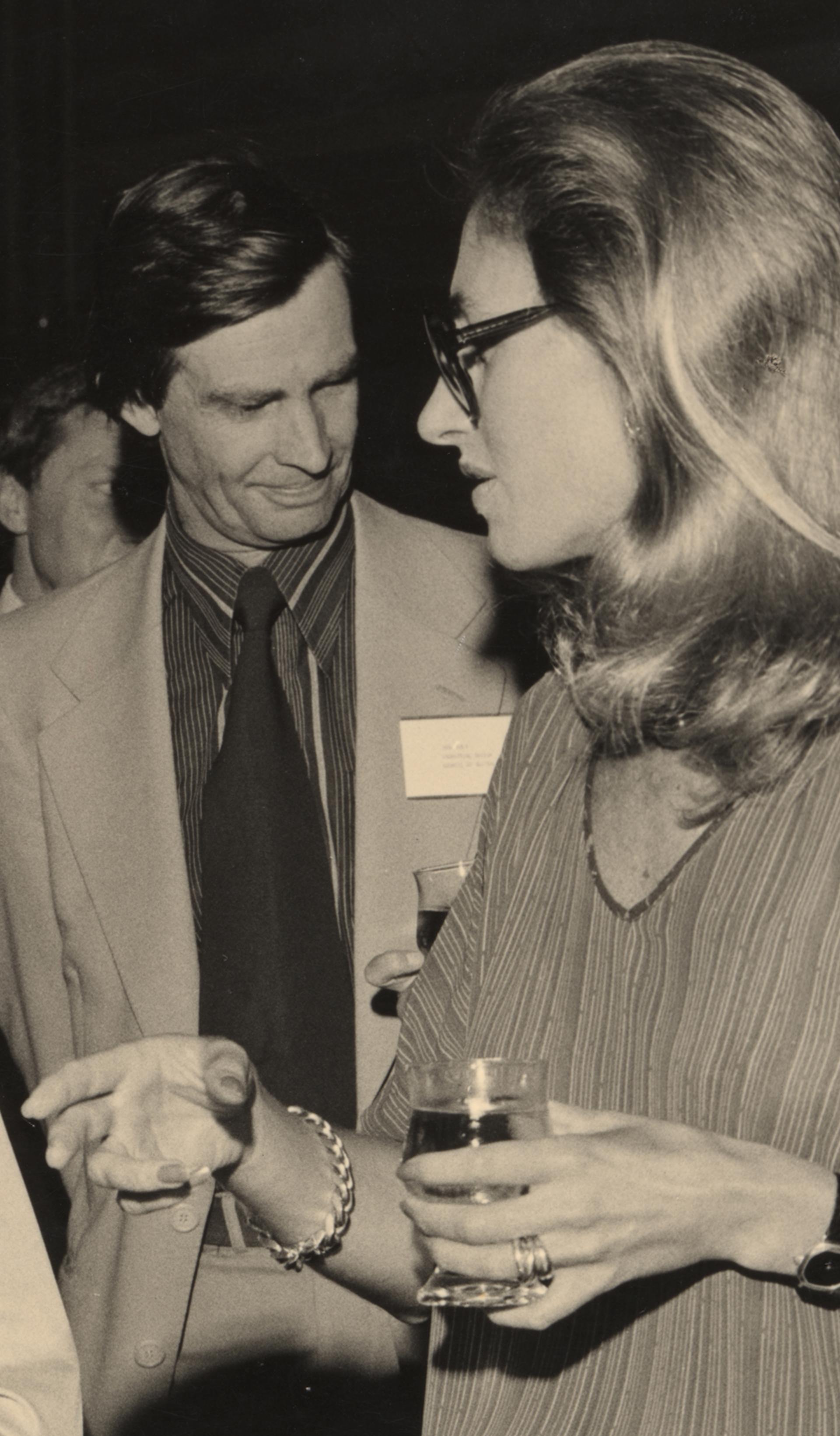A sepia-toned photograph of the design awards, in which four figures -- two men, two women -- speak together in a loose huddle, drinks in hand.