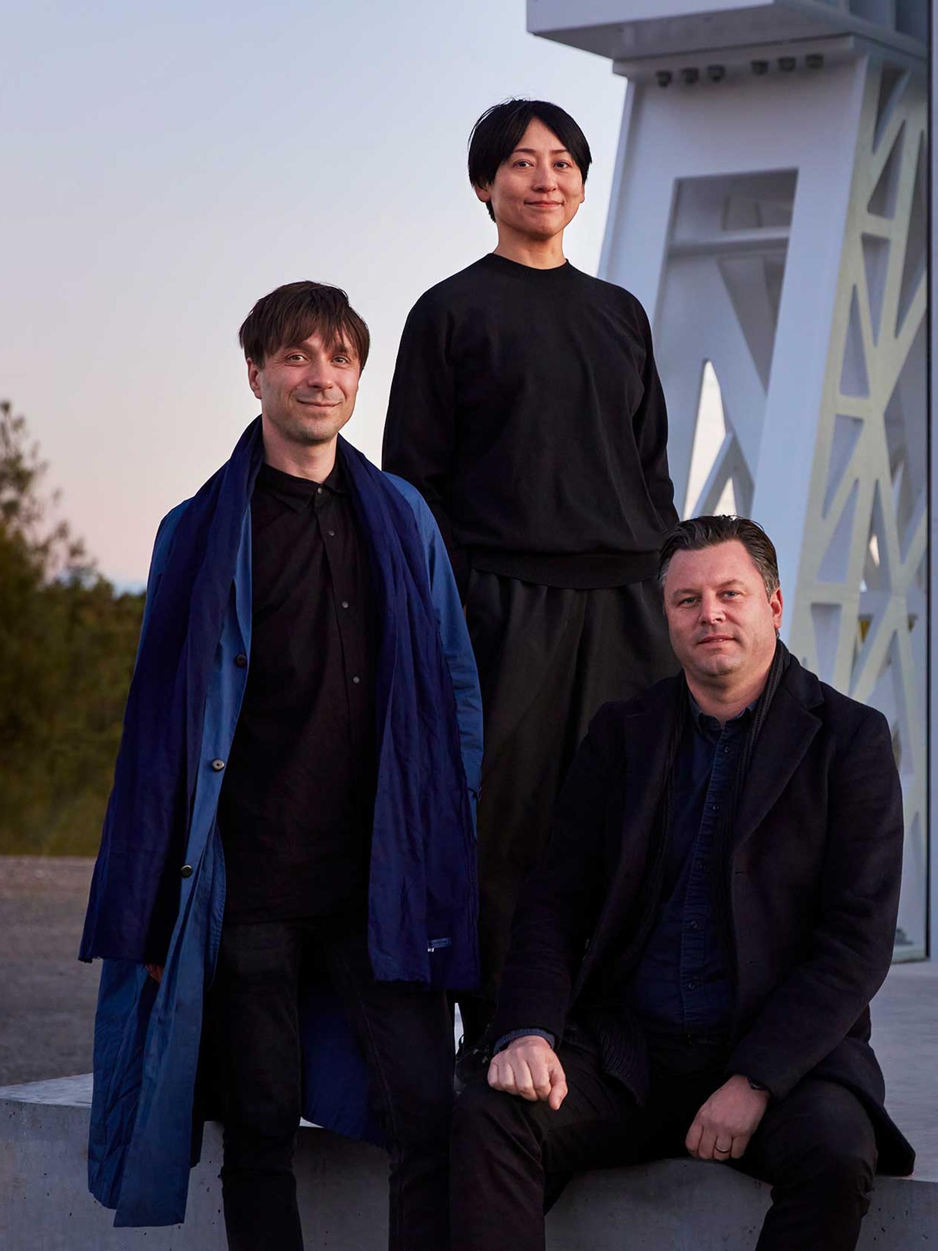 Three people (Powerhouse Parramatta architects Nicolas Moreau, Hiroko Kusunoki and Steve Toia) posed in front of a large white beam structure looking towards the camera.