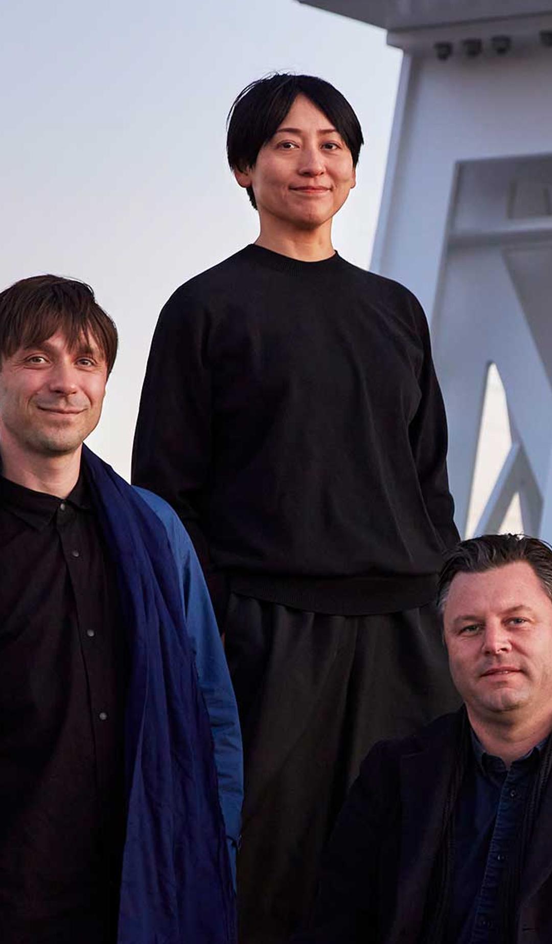 Three people (Powerhouse Parramatta architects Nicolas Moreau, Hiroko Kusunoki and Steve Toia) posed in front of a large white beam structure looking towards the camera.