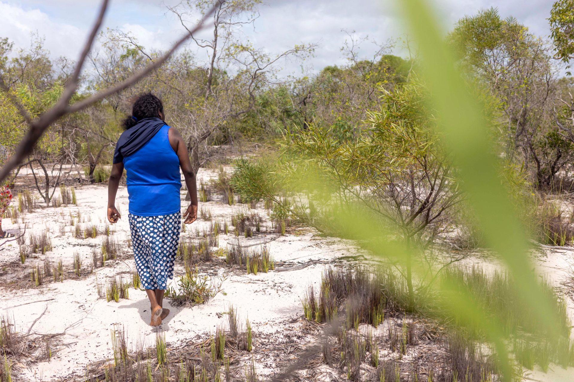 Barefoot woman walking away from camera in the sand and shrubbery