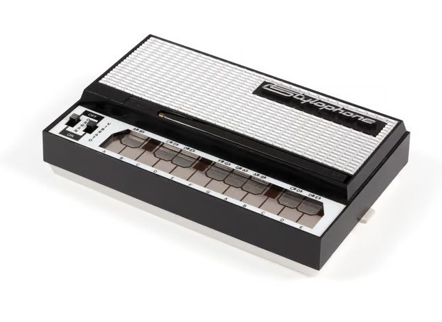 Hand-held electronic musical instrument comprising a rectangular black plastic casing with a flat silver-coloured metal keyboard.