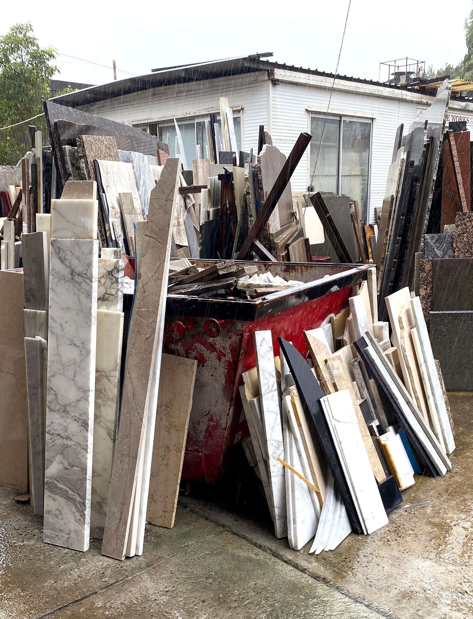 A skip outside a house with strips of scrap material leaning against it.