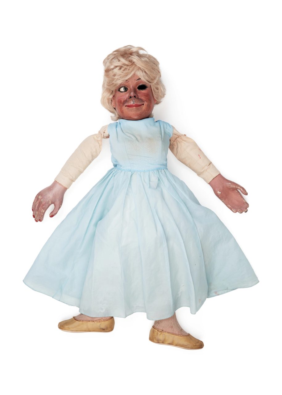 Home-made female ventriloquist's doll. The doll has a cylindrical body of plaster and cloth with a cardboard base and a plaster head, with blue eyes and a face decorated to appear as if made up with lipstick and eyeliner.