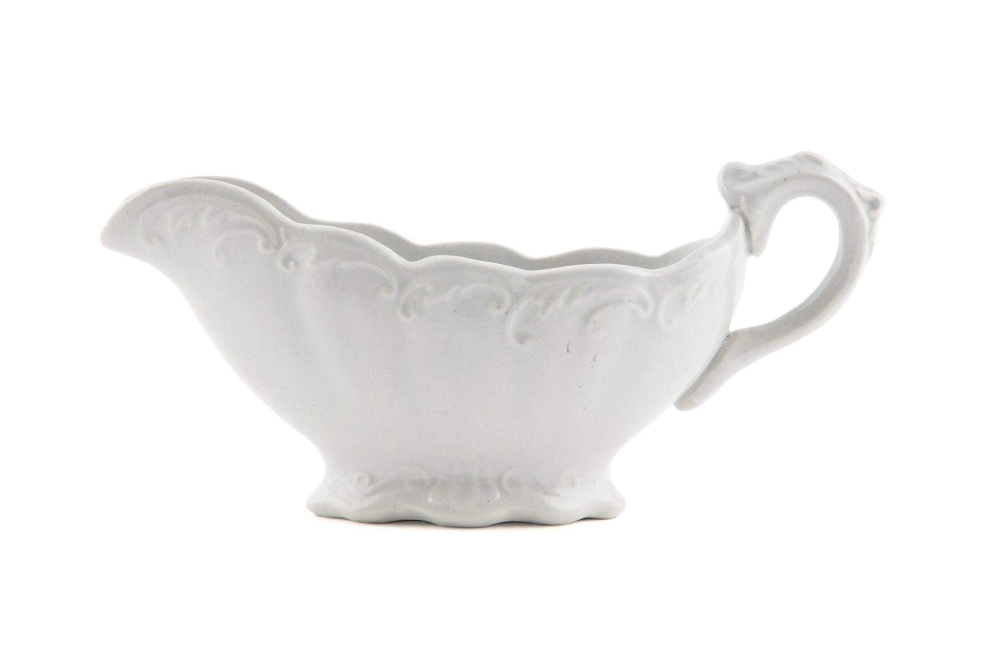 White ceramic jug, low and wide, with scalloped edging around the rim and base along with a raised swirling patterning, photographed against a white background.