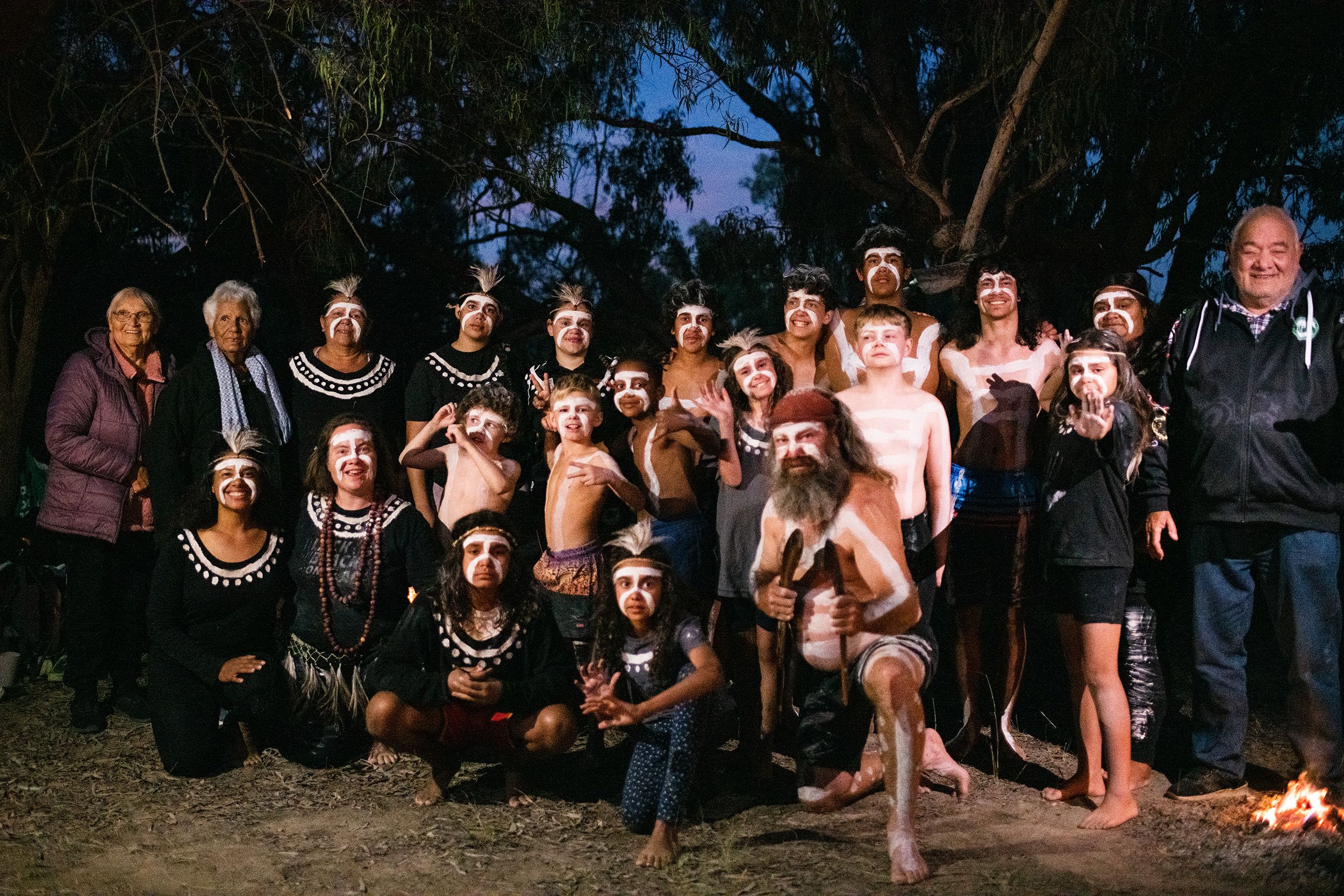 A group of Wayilwan men, women and children, some in corroboree paint, smiling at the camera.