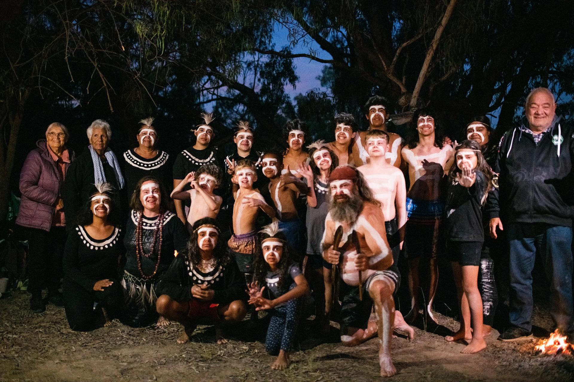 A group of Wayilwan men, women and children, some in corroboree paint, smiling at the camera.