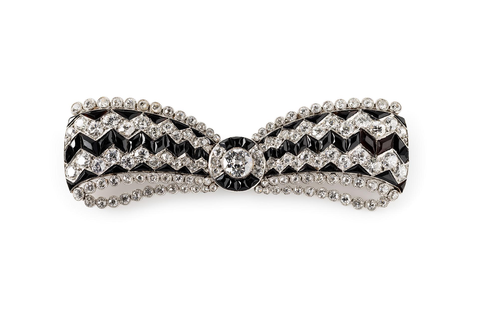 A brooch made out of white metal set with clear and black stones in a jewellery box.
